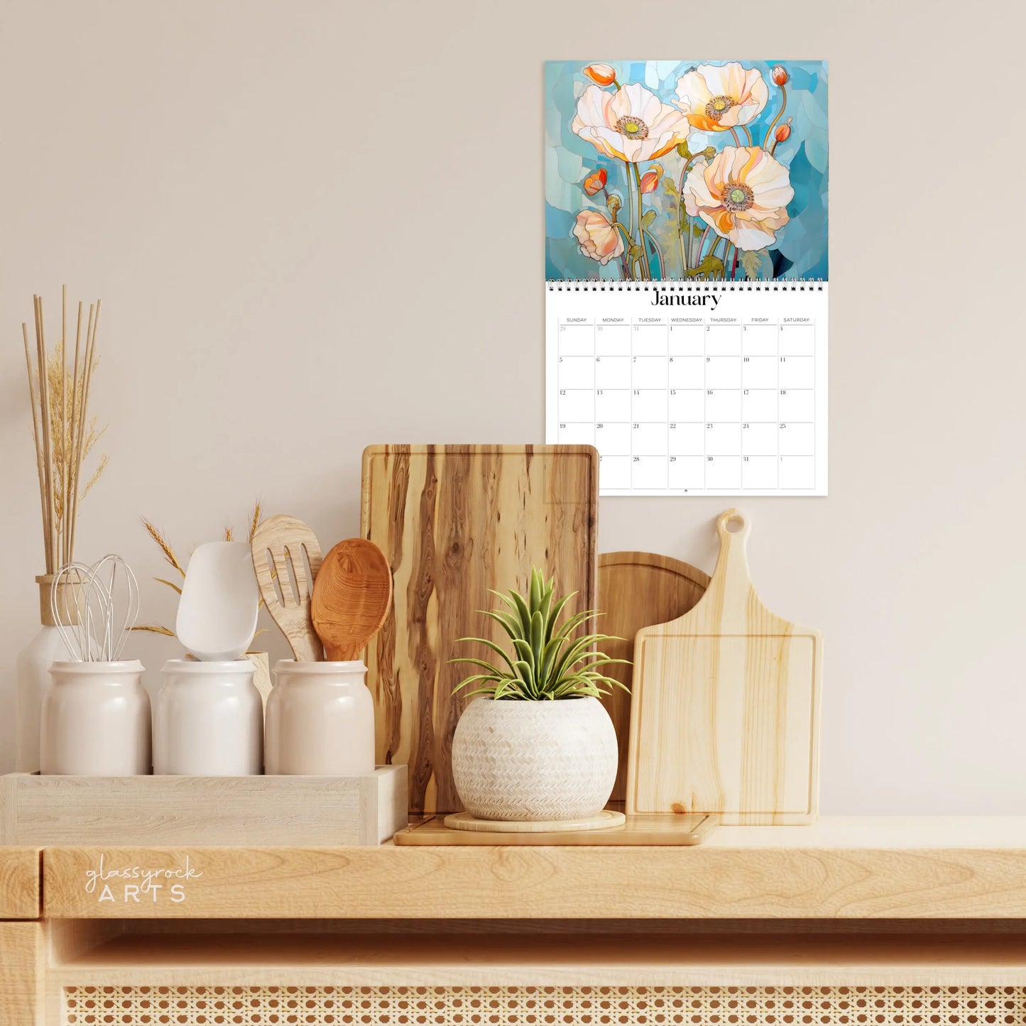 The poppies calendar hanging in a kitchen with kitchen tools below on a counter.