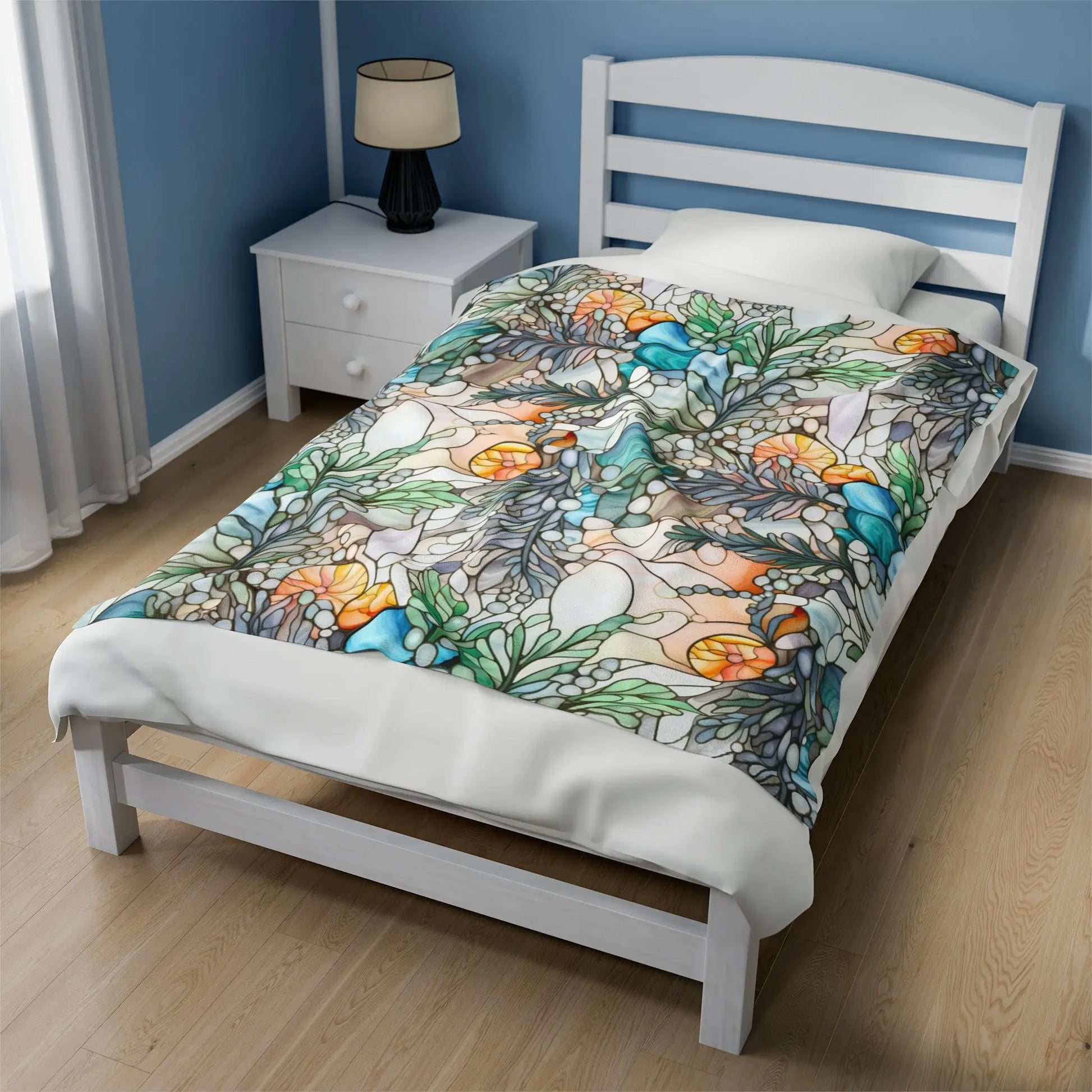 A twin bed with a white wooden frame and a Stained Glass Ferns Velveteen Soft Plush Blanket is in a room with blue walls. A white bedside table next to the bed holds a lamp with a black shade. Sunlight streams through white curtains, casting warmth over this custom creation.