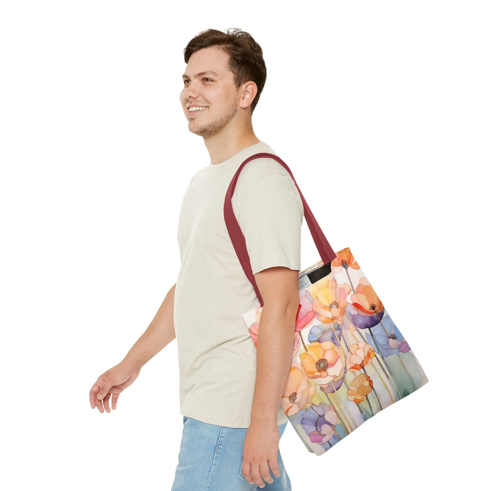 A smiling person with short hair wears a light green shirt and blue jeans, carrying the Stained Glass Poppy Flowers Tote Bag over their shoulder. The colorful tote, featuring maroon handles and crafted from durable polyester, stands out against the plain white background.