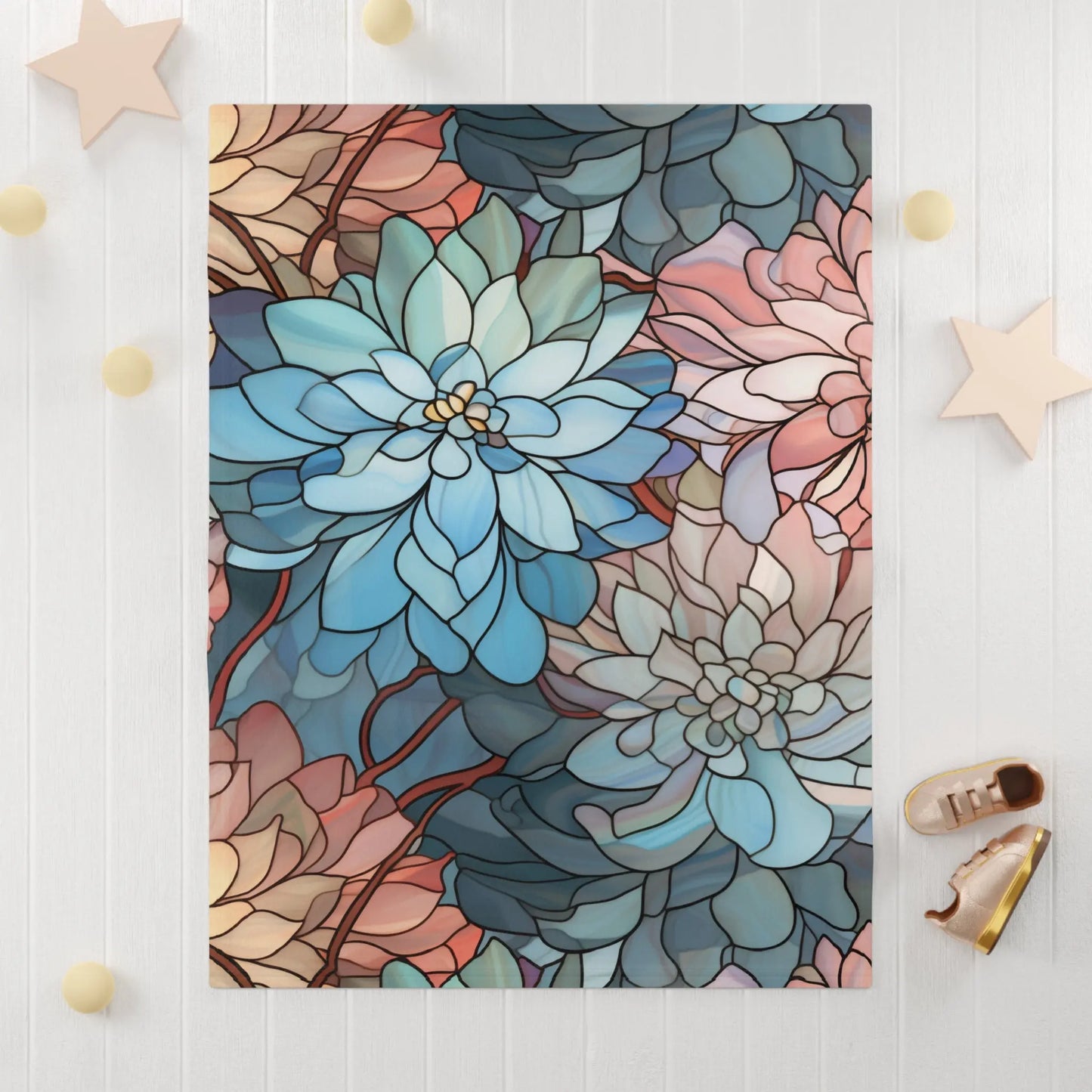 A stunning boho-style baby blanket showcases a vibrant stained glass design of blue, pink, and beige flowers with intricate petal details. Positioned on a white surface, its adorned with small decorative stars and cream-colored balls. Product: Stained Glass Dark Flowers Soft Fleece Baby Blanket.