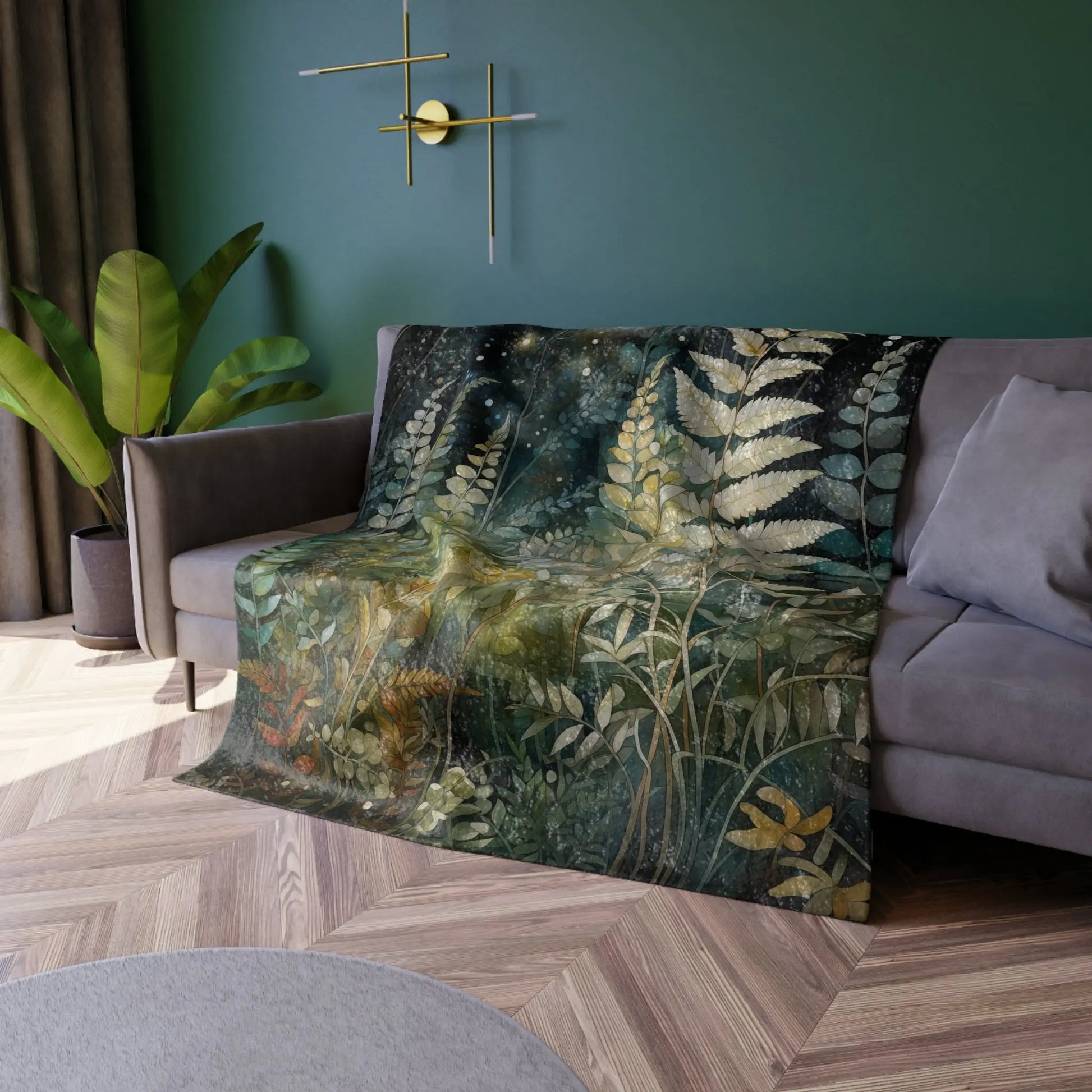 A cozy living room showcases a gray sofa adorned with the Stained Glass Midnight Ferns Crushed Velvet Blanket, featuring ferns and leaves. Green walls with minimalist golden decor, lush corner plants, and an elegant stained glass design cast colorful patterns throughout.