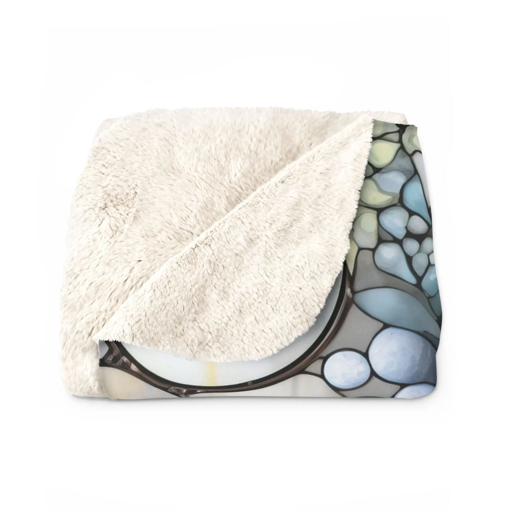 The Stained Glass Nouveau Ferns Sherpa Fleece Blanket is a folded plush velveteen blanket with a cream-colored side and a boho stained glass pattern of rounded stones in blue, green, and gray.