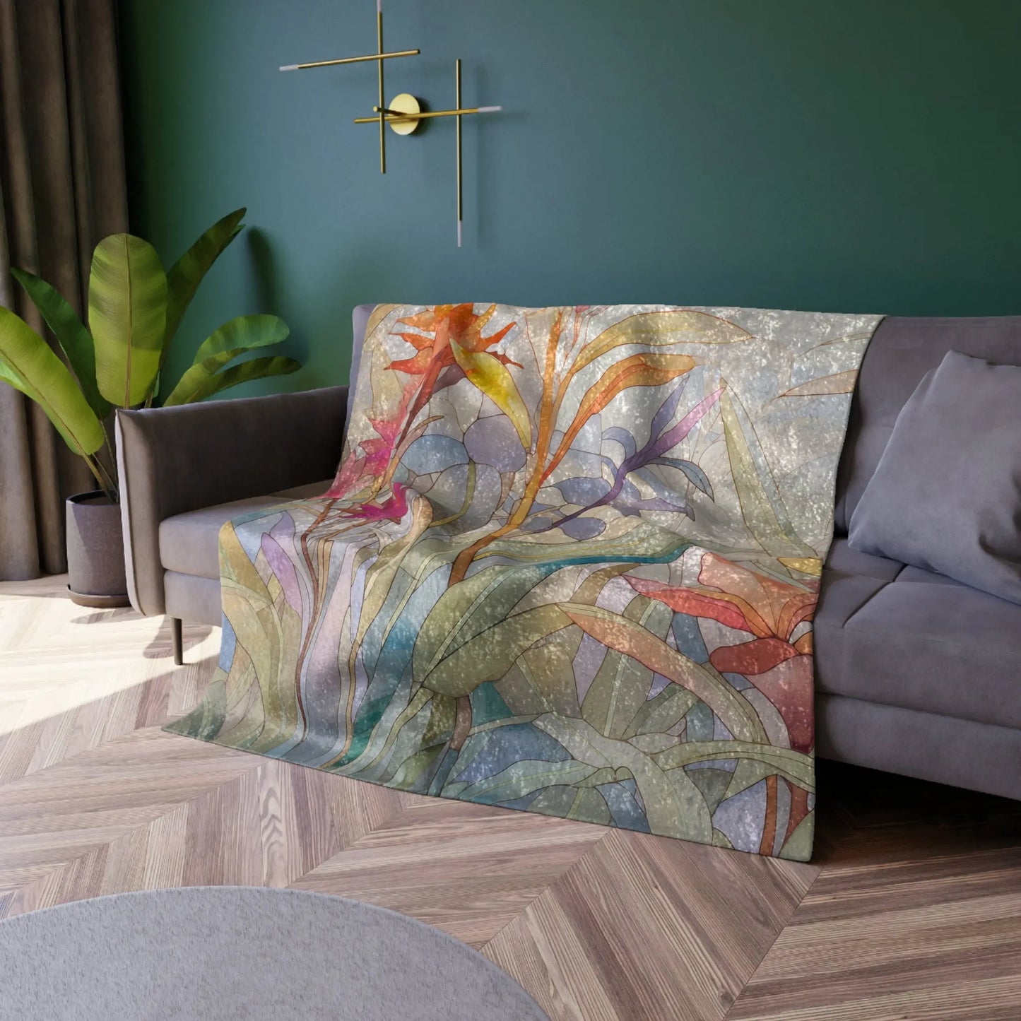 A sofa with a Stained Glass Tropical Flowers Crushed Velvet & Fleece Blanket draped over it sits in a room with dark green walls. Above, a modern wall sconce adds light, and a potted plant brings nature indoors. The floor features an elegant herringbone wood pattern.