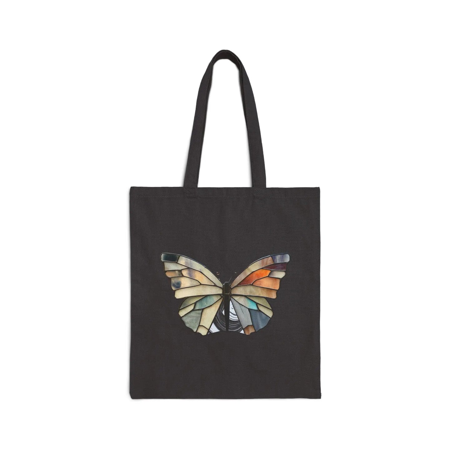The Stained Glass Summer Butterfly Cotton Canvas Tote Bag by Noelle Barnes features a butterfly with wings resembling a stained glass design in blue, orange, and beige mosaic, set against a plain black background that highlights the intricate artistry.