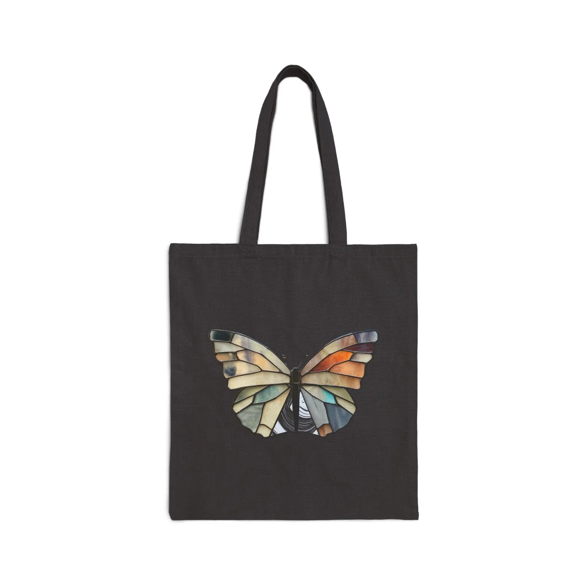 The Stained Glass Summer Butterfly Cotton Canvas Tote Bag by Noelle Barnes features a butterfly with wings resembling a stained glass design in blue, orange, and beige mosaic, set against a plain black background that highlights the intricate artistry.