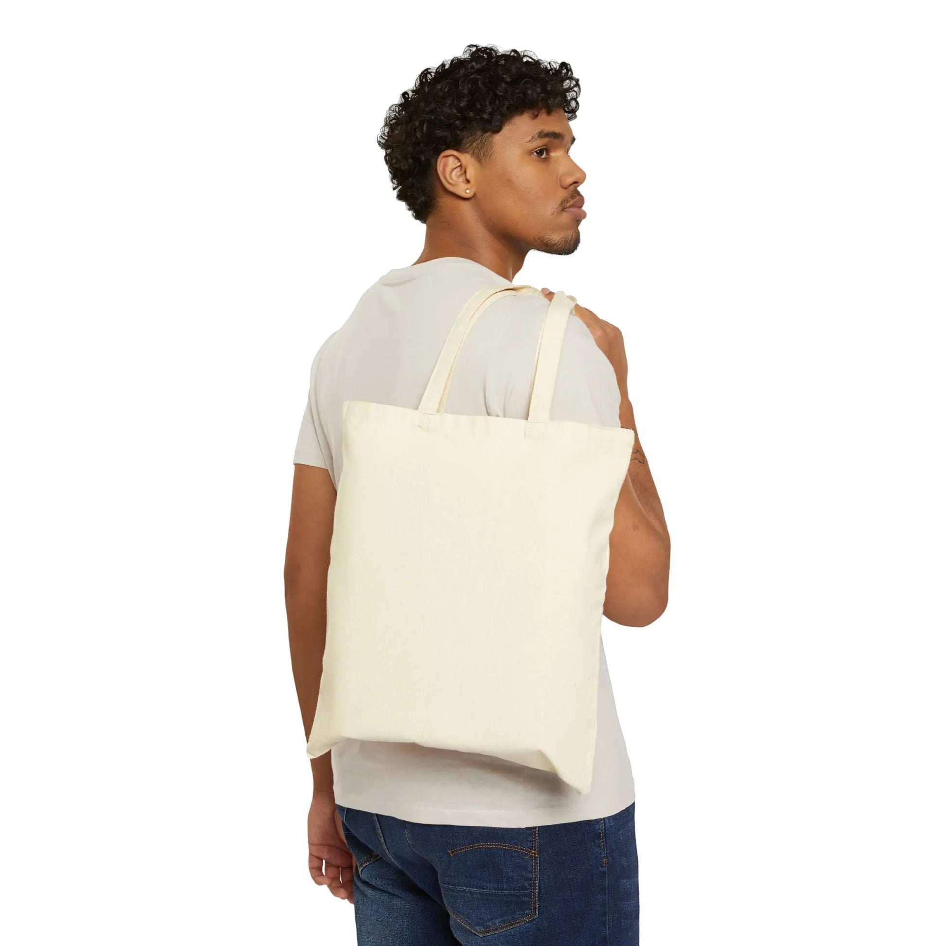 A person with curly hair wears a light gray t-shirt and blue jeans, holding the Stained Glass Seagull Cotton Canvas Tote Bag over their shoulder. They are glancing sideways against a plain white background.