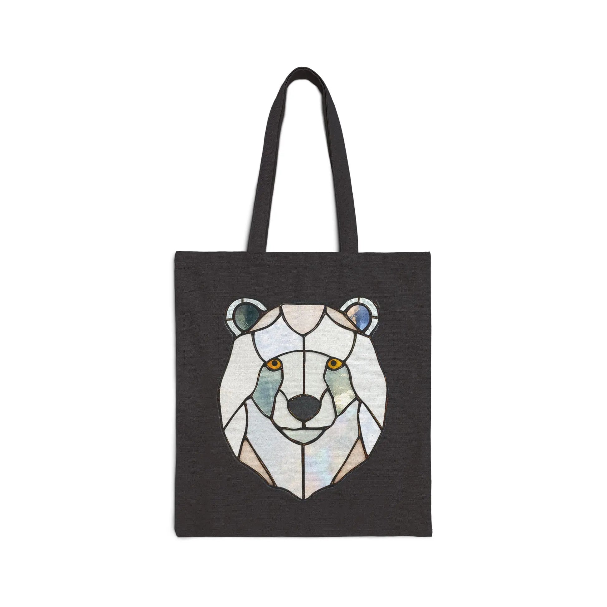 The Stained Glass Polar Bear Cotton Canvas Tote Bag by Noelle Barnes features a geometric polar bear design in shades of white, blue, and gray, with striking orange eyes that contrast beautifully against the pattern.