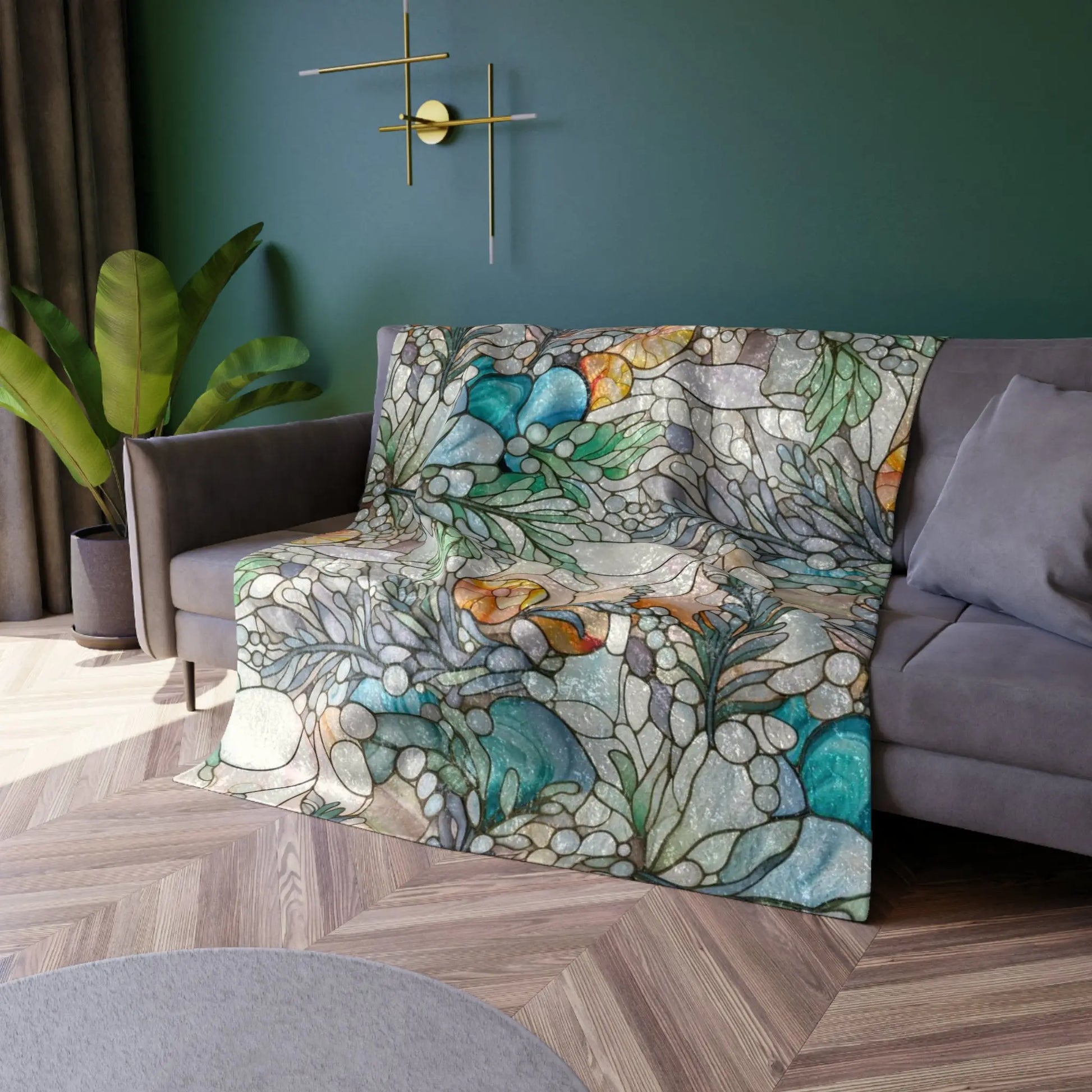 The Stained Glass Rainbow Ferns Forest Crushed Velvet Blanket, draped over a sofa, adds vibrant color against a dark green wall with a modern gold lamp. A potted plant stands beside the couch, and part of a gray crushed velvet rug is visible on the wooden floor.