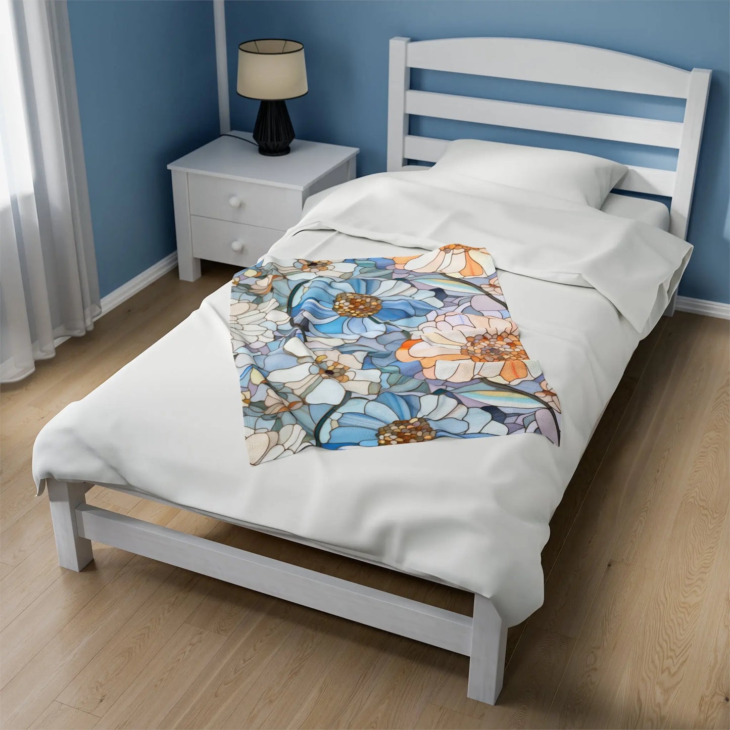 A white bed with a wooden frame is adorned in crisp white sheets, topped with the Stained Glass Flowers Plush Blanket showcasing a floral design in blue, orange, and brown. A lamp rests on a bedside table beside the bed, enhancing the charm of this cozy retreat.