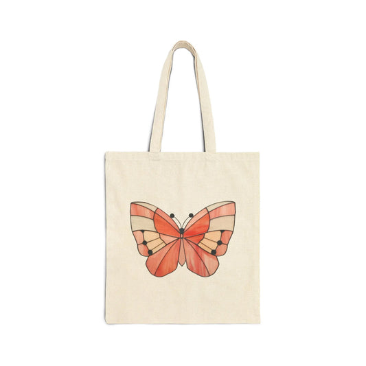 The Stained Glass Spring Butterfly Cotton Canvas Tote Bag features a cream-colored design with an orange butterfly and black accents on its wings, reminiscent of stained glass, set against a white background.