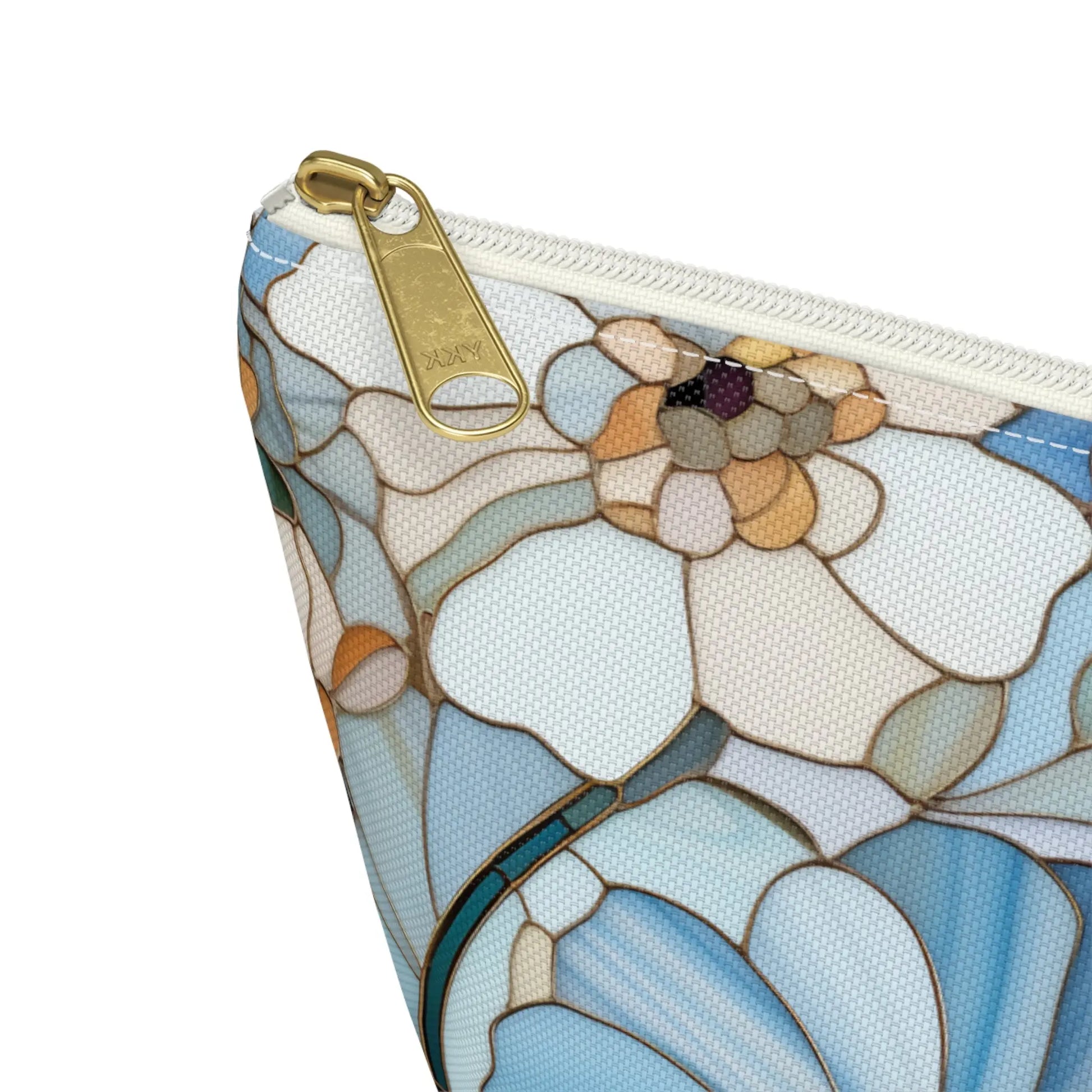 A close-up of the Stained Glass Flowers Cosmetic Bag showcases a bohemian floral pattern in blue, white, and beige. It includes a gold zipper with a SMRITI stamped metal pull tab and intricate abstract flower petal details.