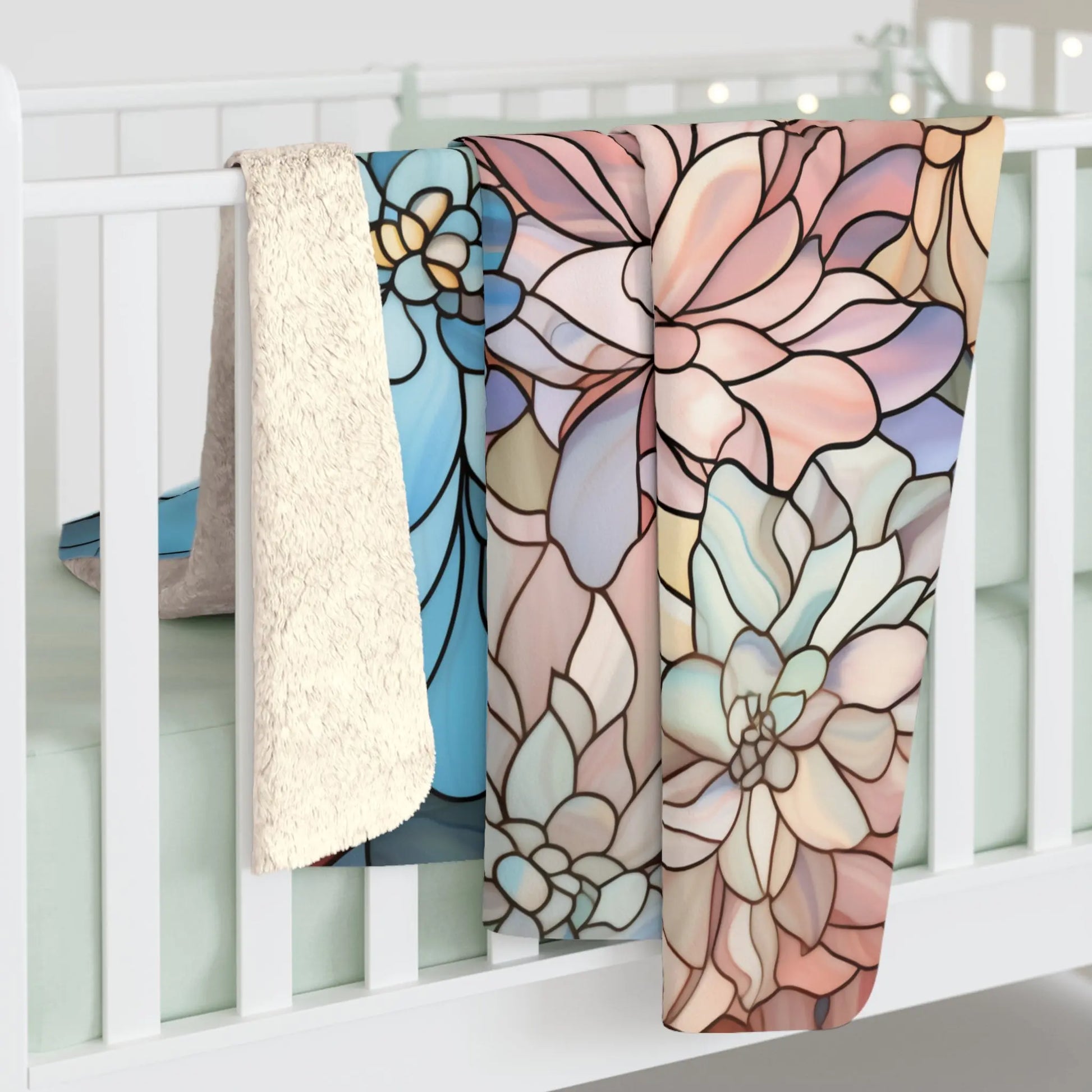 Three vibrant boho blankets, including the Stained Glass Dark Flowers Sherpa Fleece Blanket, drape over a white crib railing. They showcase floral patterns in blue, peach, and pink hues. Soft lights in the background create a cozy glow in this plush velveteen setting.