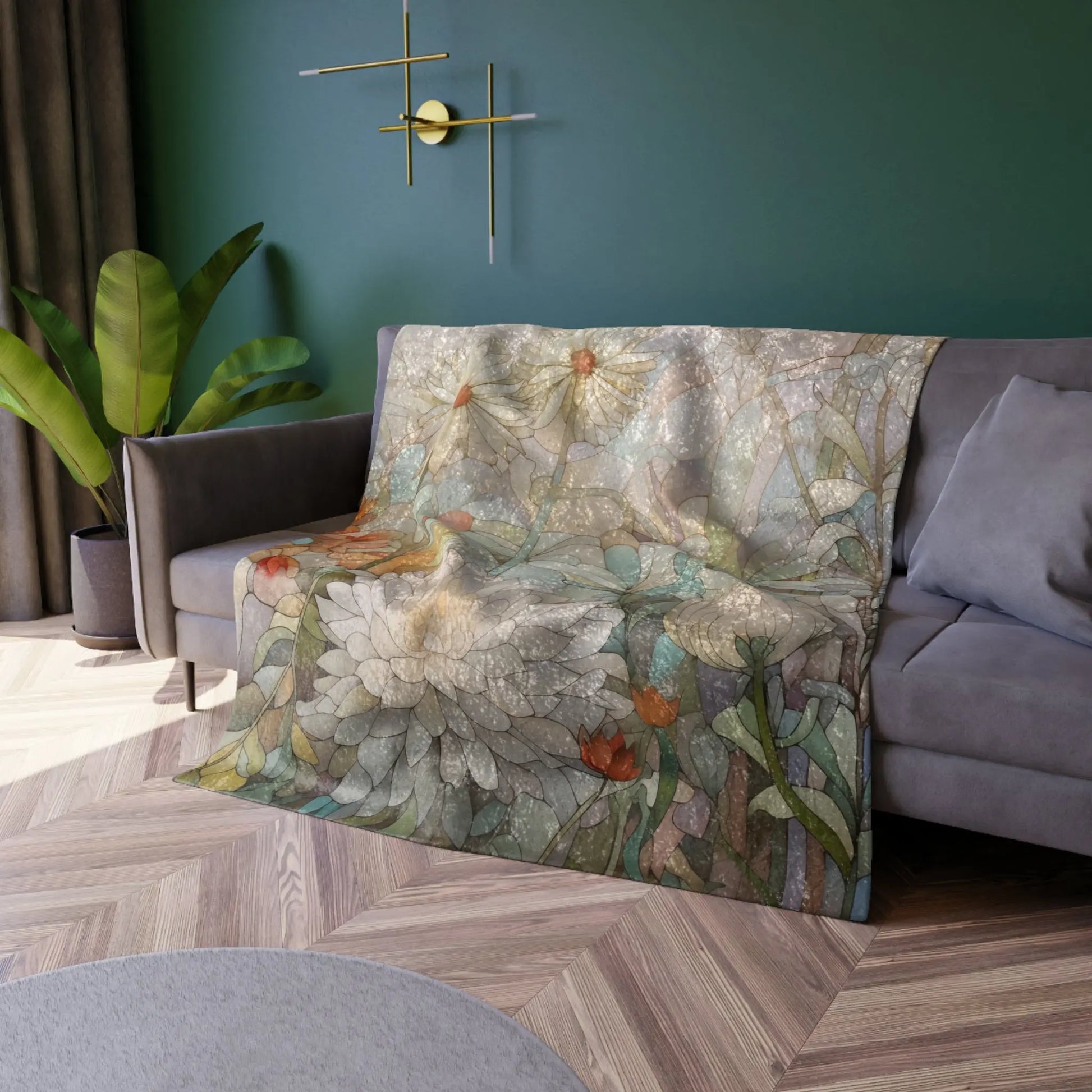 A sofa in a modern living room features a floral throw with large white and orange flowers against a dark green wall. A gold geometric wall decoration, leafy plant, and the Stained Glass Spring Flowers Crushed Velvet & Fleece Blanket - 50x60 enhance the space.