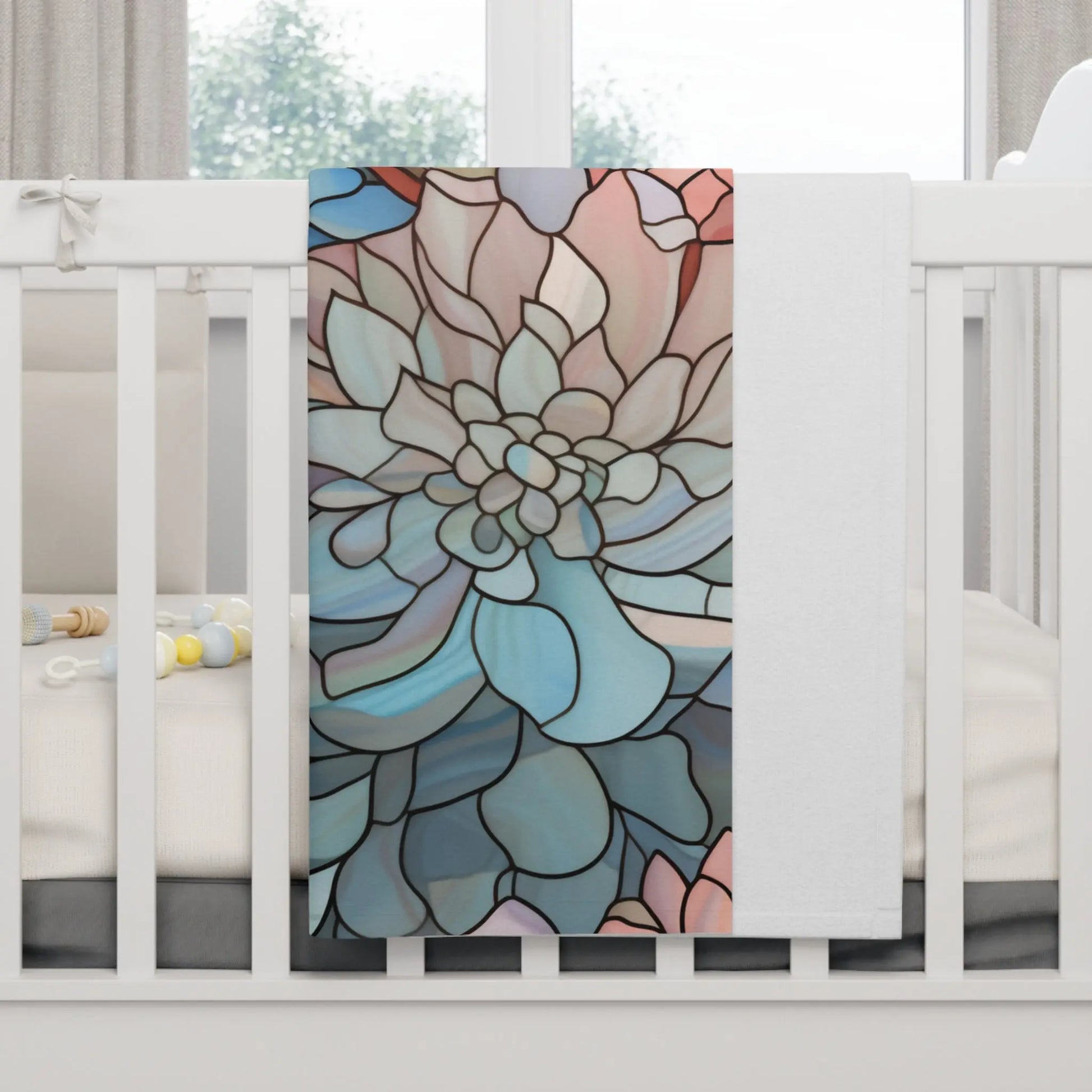 A crib with the Stained Glass Dark Flowers Soft Fleece Baby Blanket draped over the side showcases a floral design in blue, pink, and beige. Inside are baby toys and a soft cushion, all exuding boho elegance.