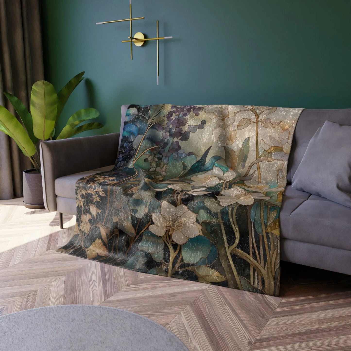 A cozy living room with a dark green wall, gray sofa, and plant beside it. The Stained Glass Midnight Flowers crushed velvet blanket in earthy tones is draped over the sofa, while a modern gold light fixture adds warmth and style to the space.