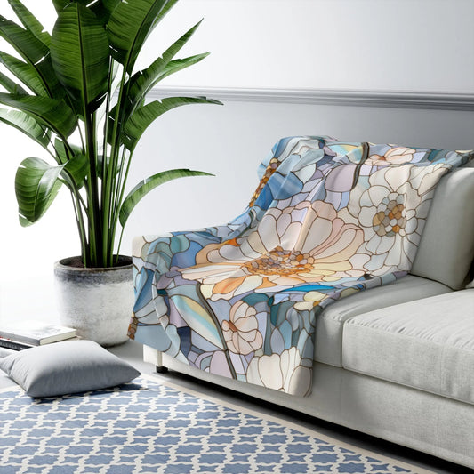 A light-colored sofa with a Stained Glass Flowers Sherpa Fleece Blanket exudes boho elegance next to a tall potted plant. A gray throw pillow and geometric-patterned rug complement the space in this well-lit, modern setting.