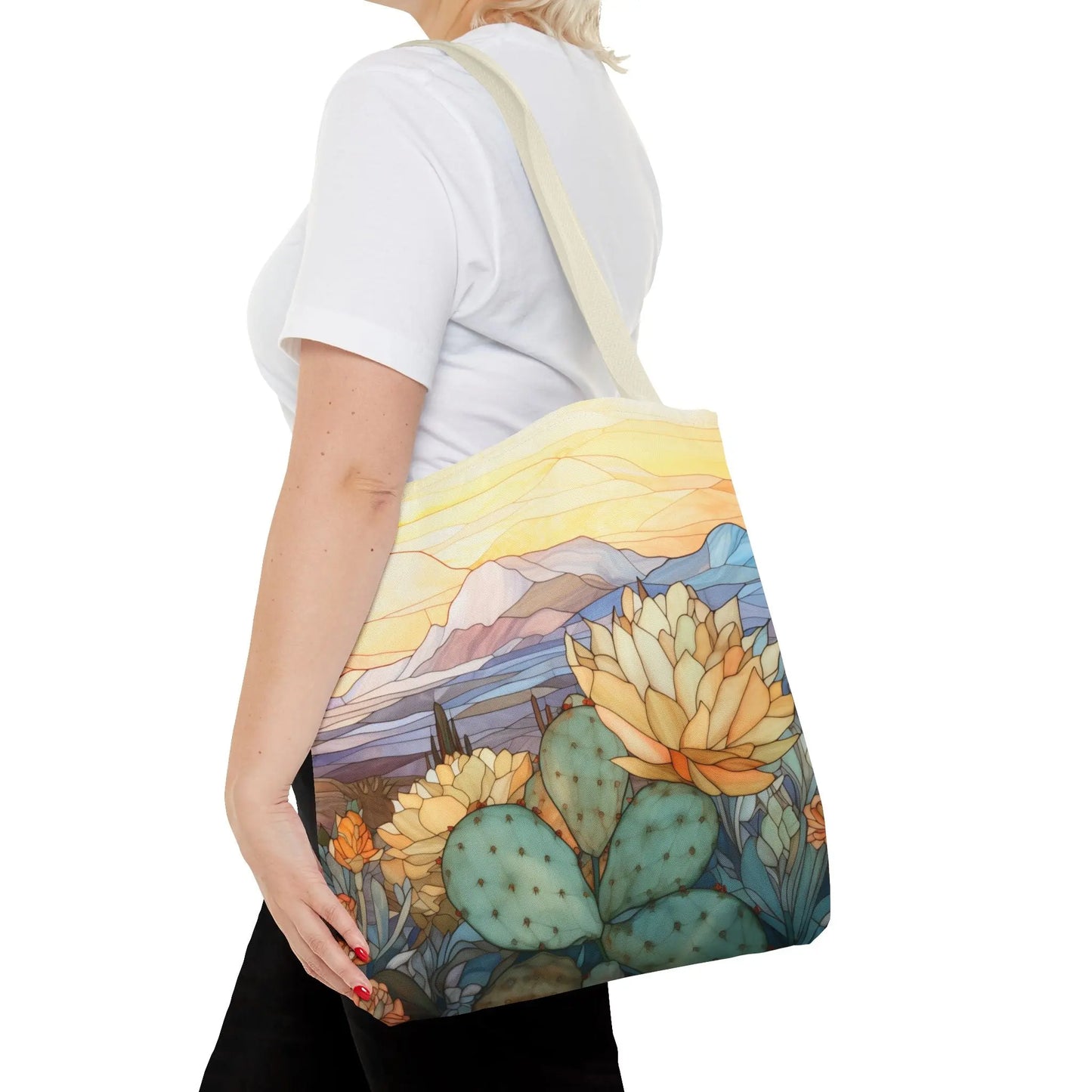 A person in a white t-shirt carries a Stained Glass Desert Cactus Tote Bag made from durable polyester, featuring an original artist design of blooming cacti and a desert landscape under a colorful sky.