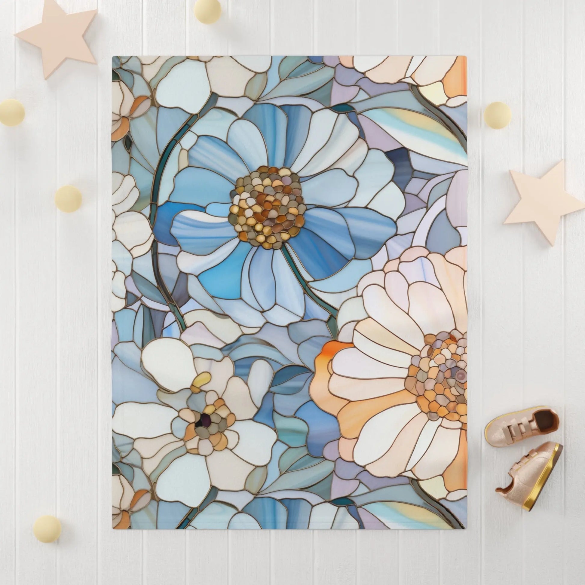 The Stained Glass Flowers Soft Fleece Baby Blanket, showcasing large blue, white, and peach flowers on a light background, exudes boho elegance. Placed on a white table with decorative stars and small balls around it, this custom creation is complemented by brown shoes nearby.