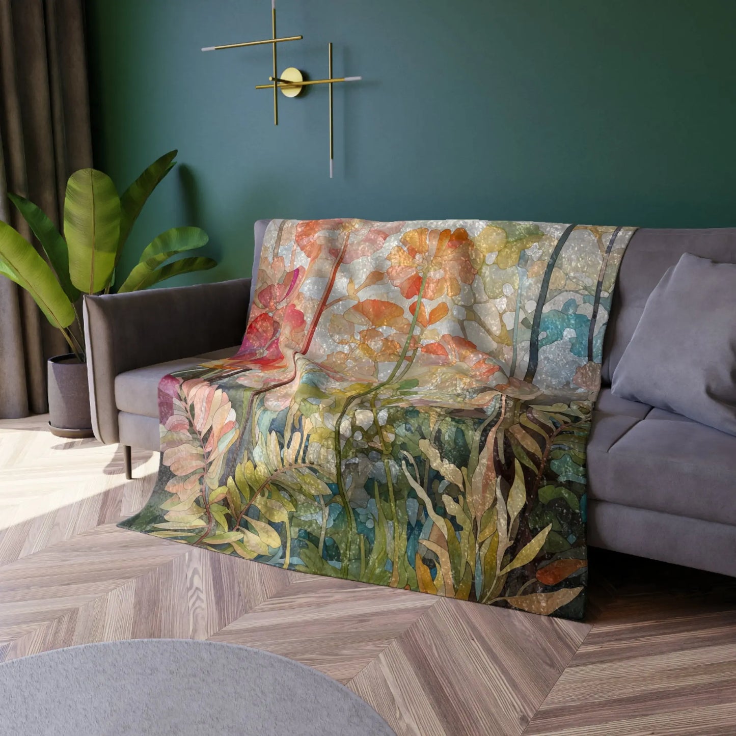 A cozy room features a gray sofa with a Stained Glass Flowers & Ferns Crushed Velvet and Soft Fleece Blanket draped over it. The green wall is adorned with a modern gold lamp, while a potted plant complements dark curtains and light wood flooring beautifully.