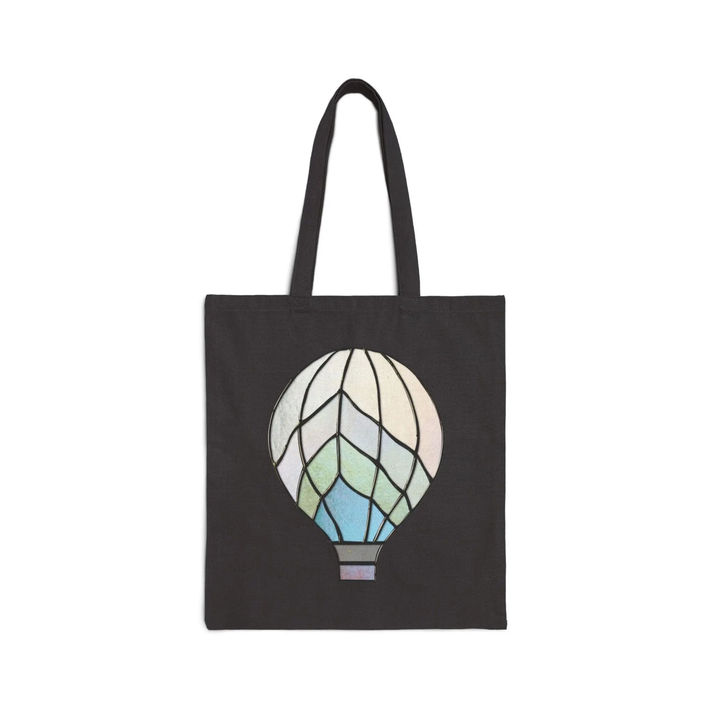 The Stained Glass Hot Air Balloon Cotton Canvas Tote Bag is a black canvas bag with a vibrant design of a hot air balloon in blue, green, and white mosaic-like patterns on the front, made from 100% cotton.