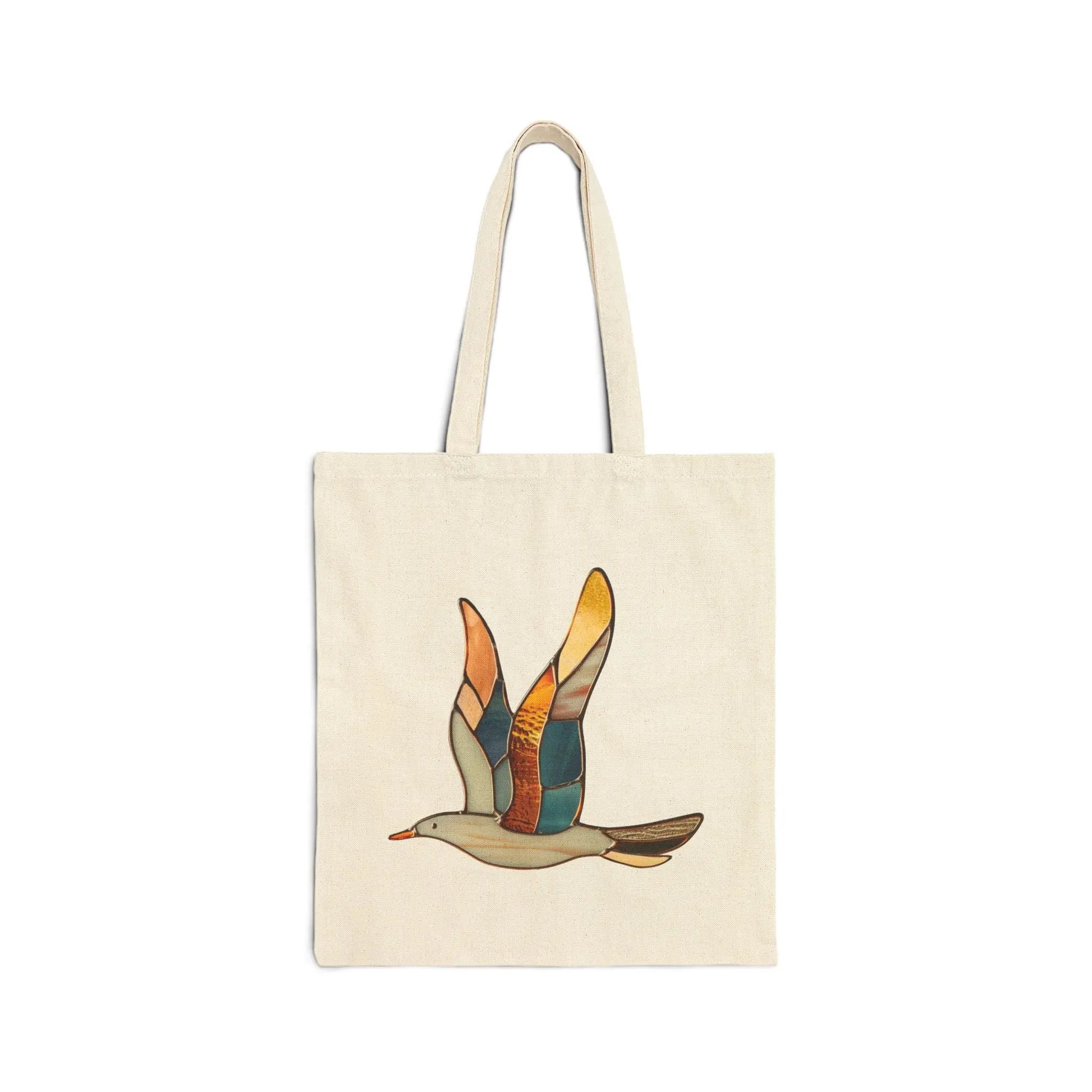 The Stained Glass Seagull Cotton Canvas Tote Bag by Noelle Barnes is beige and features a stylized bird in flight with wings displaying sections of orange, yellow, teal, and brown like a stained glass design.