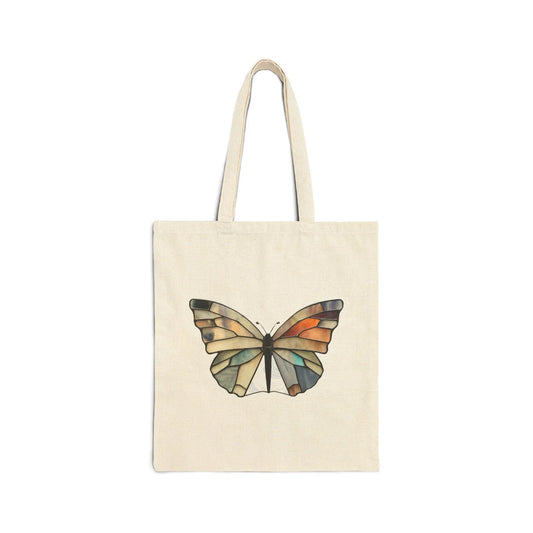 The Stained Glass Summer Butterfly Cotton Canvas Tote Bag, designed by Noelle Barnes, showcases a colorful butterfly with geometric orange, green, and blue patterns on a beige canvas. It features two sturdy handles and is attractively presented against a white backdrop.