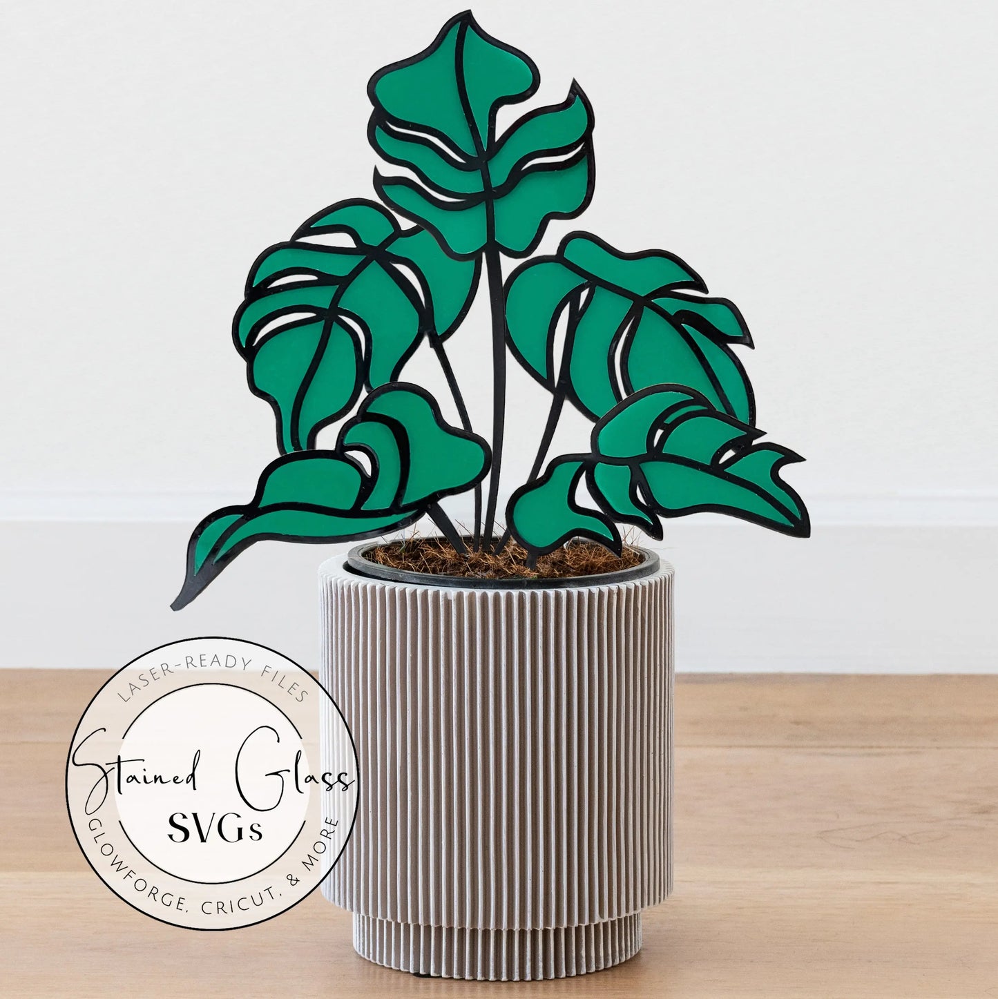 Illustration of a potted plant with stylized monstera leaves, resembling stained glass art. The plant is in a ribbed gray pot on a wooden surface. A circular logo reads Five Stained Glass Monstera Leaf Stem SVGs and mentions Glowforge project files for crafting.
