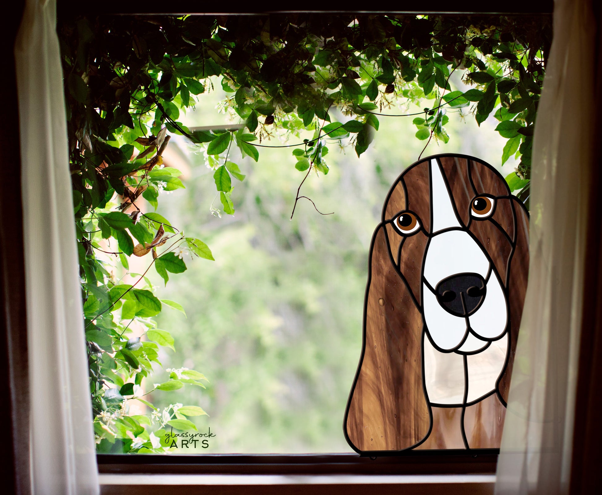 This Basset Hound Dog Stained Glass Pattern showcases a charming dog suncatcher with floppy ears amidst lush green leaves. Its curious and friendly look makes it a perfect gift for dog lovers.