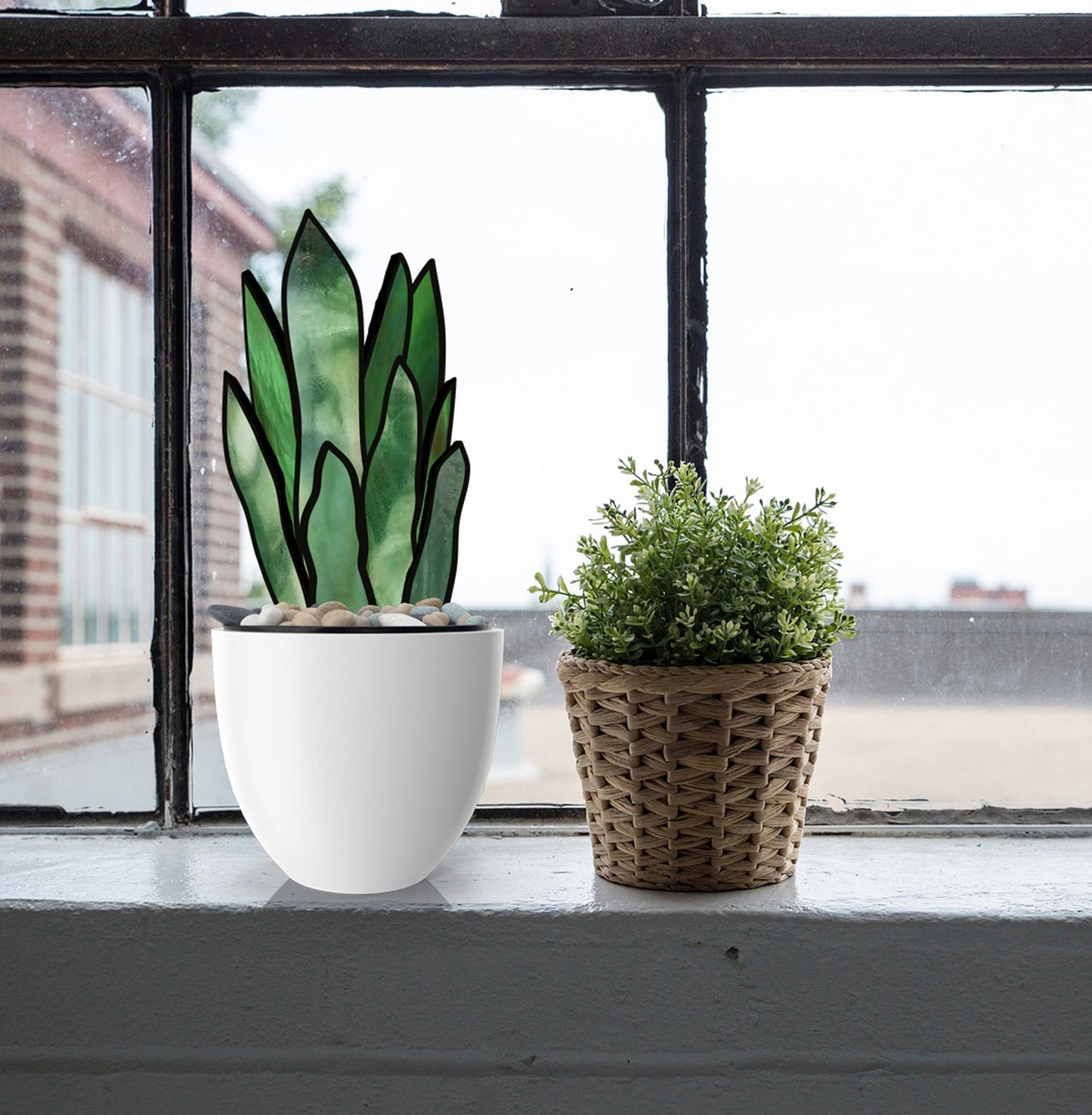 A white pot with decorative green leaves and pebbles rests beside a small woven basket holding a leafy green plant on a window sill. Through the window, blurred buildings and cloudy skies are visible, echoing the intricate pattern of 3D Snake Plant Leaves Stained Glass Pattern.