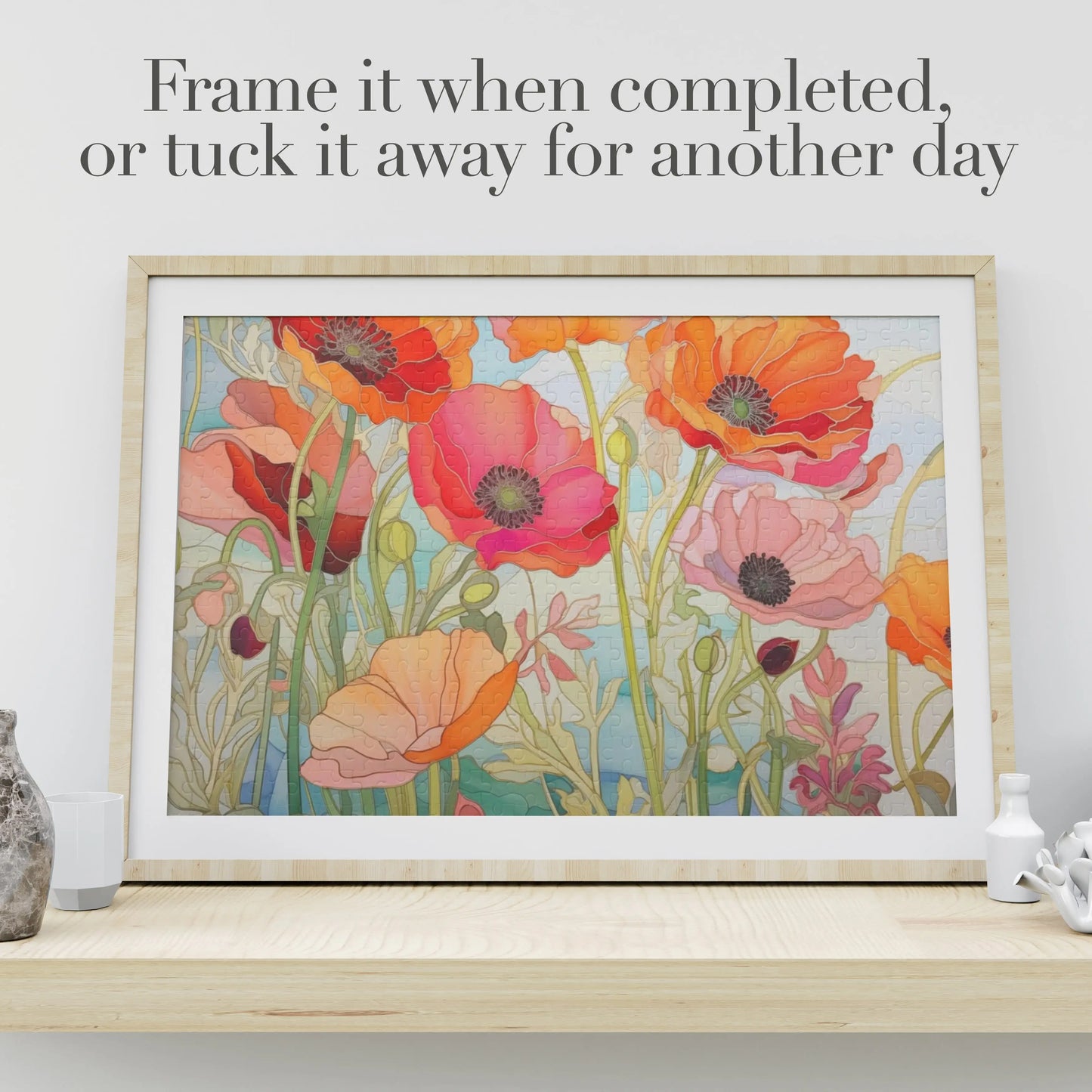 The California Poppies Jigsaw Puzzle features vibrant orange and pink poppies on a wooden shelf. Text reads, Frame it when completed, or tuck it away for another day. A small vase and white decorative object enhance this stained glass-inspired art gift.