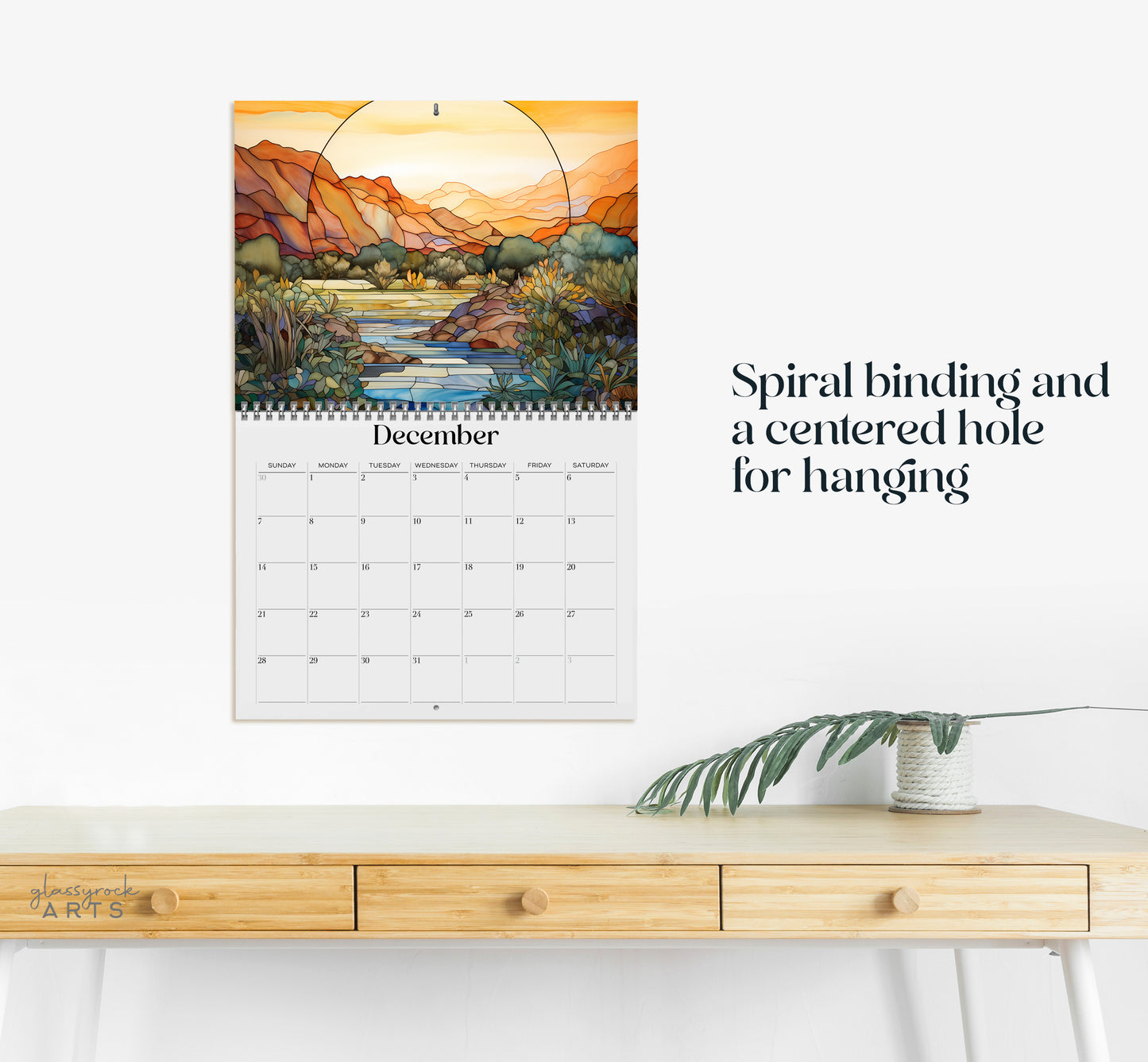 The 2025 Wall Calendar - Stained Glass Desert Landscapes, with spiral binding and a centered hole for hanging, features vivid desert illustrations.