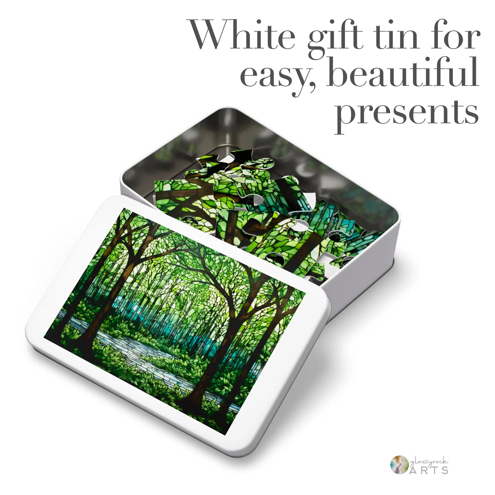 A white gift tin with a green stained glass forest scene, similar to the Stained Glass Forest Jigsaw Puzzle. The partially open lid reveals a matching pattern inside. Text states, White gift tin for easy, beautiful presents.”.