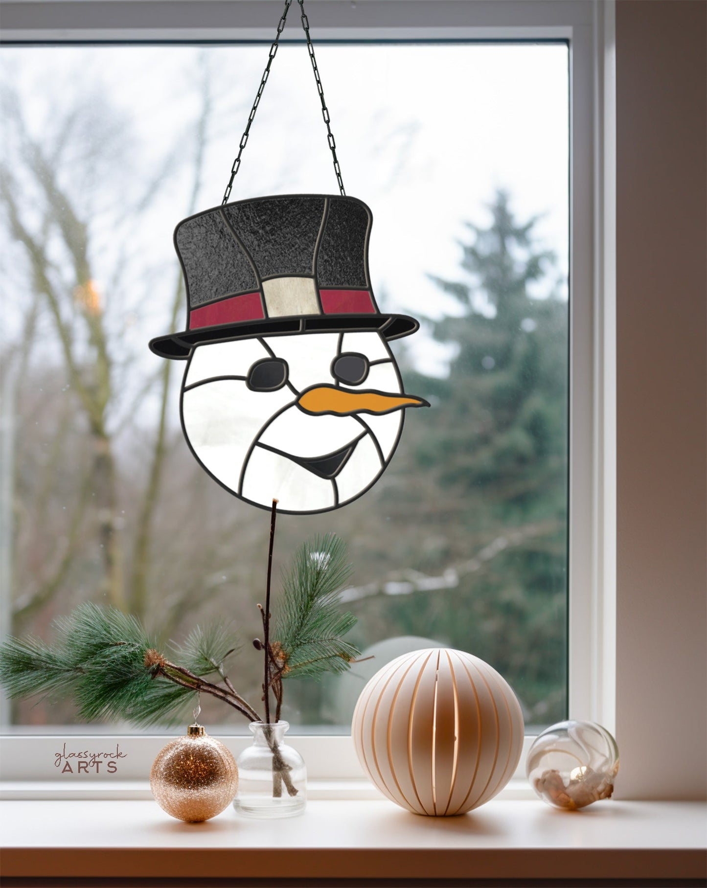 The Snowman Stained Glass Pattern featuring a top hat and orange nose brings charm to festive decor. A pine branch with golden, white, and transparent spheres enhances the windowsill, while outdoor trees add natural beauty—ideal for Christmas pattern enthusiasts.