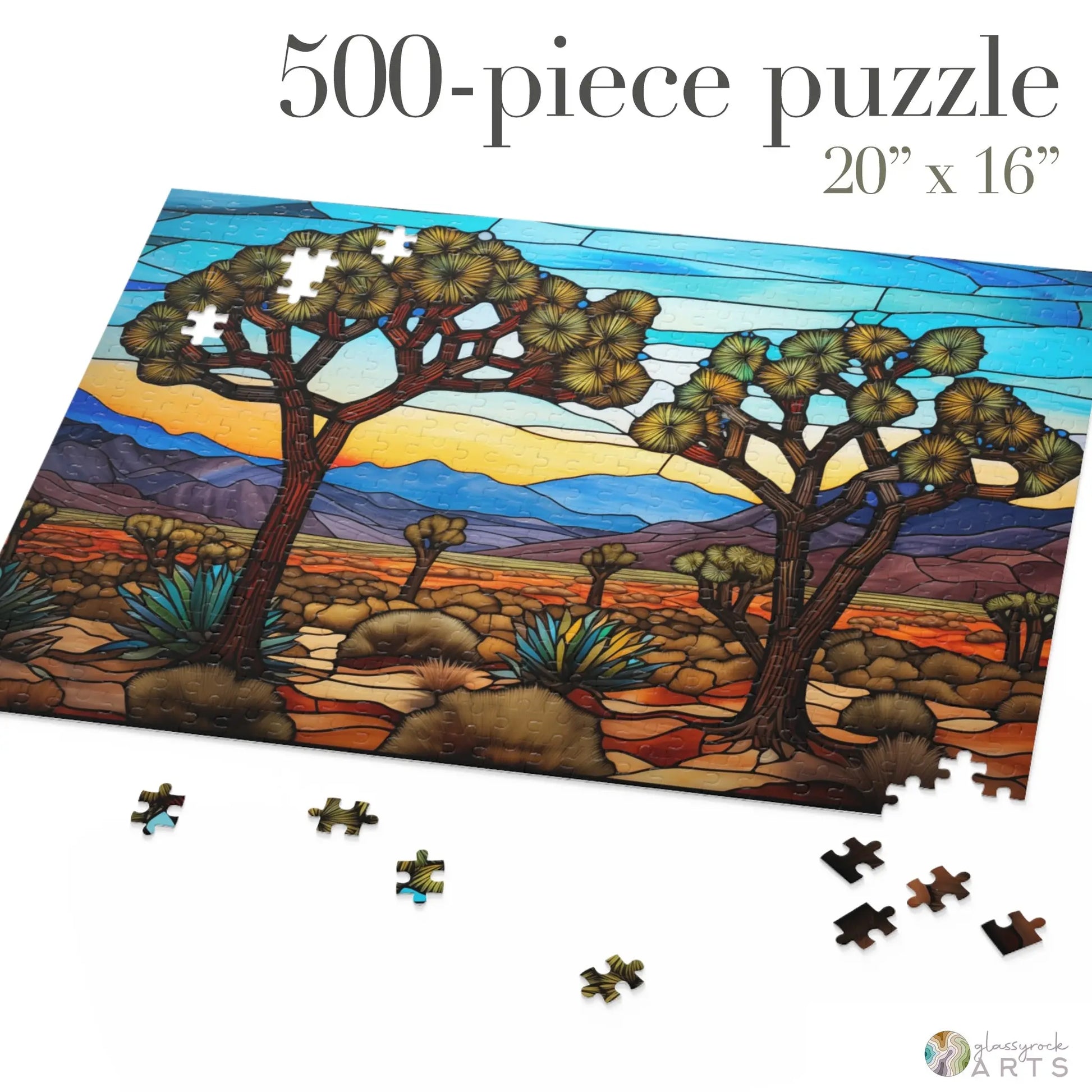 The Joshua Tree National Park Jigsaw Puzzle, a 500-piece set measuring 20x16, showcases a desert landscape with two large trees, mountains, and a vivid sky. Some pieces are missing or scattered on a white surface, resembling an unfinished stained glass scene.