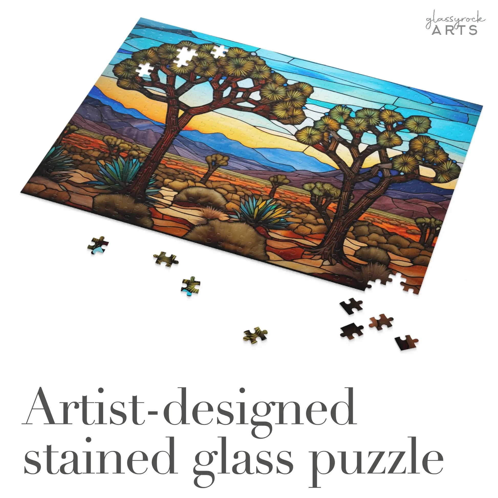The Joshua Tree National Park Jigsaw Puzzle portrays a vibrant desert scene with majestic trees and mountains in the background. Scattered puzzle pieces await assembly. The text, Artist-designed stained glass puzzle, makes it an ideal art gift.