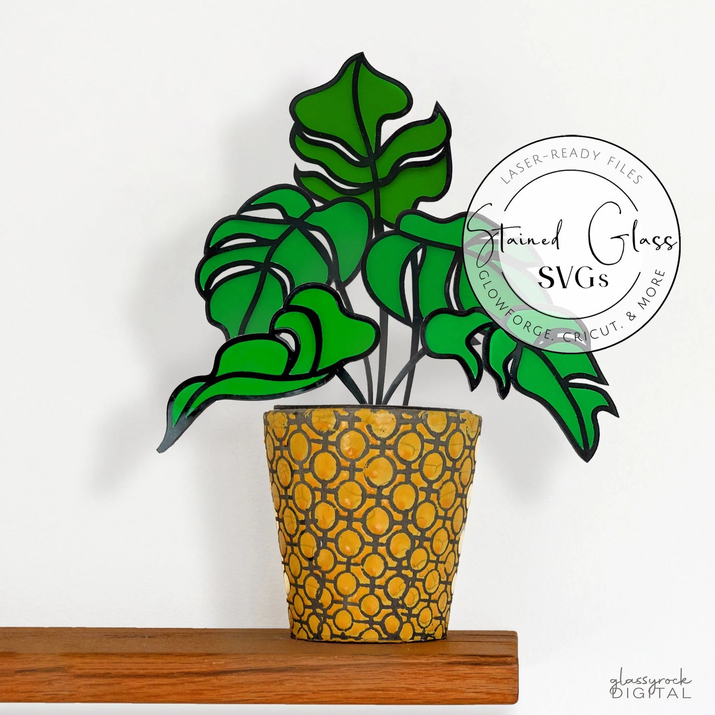 A vibrant stained glass art of green monstera leaves in a patterned pot on a wooden shelf, featuring a circular Stained Glass SVGs label. Compatible as a laser cut file, ideal for Glowforge projects. Product: Five Stained Glass Monstera Leaf Stem SVGs.