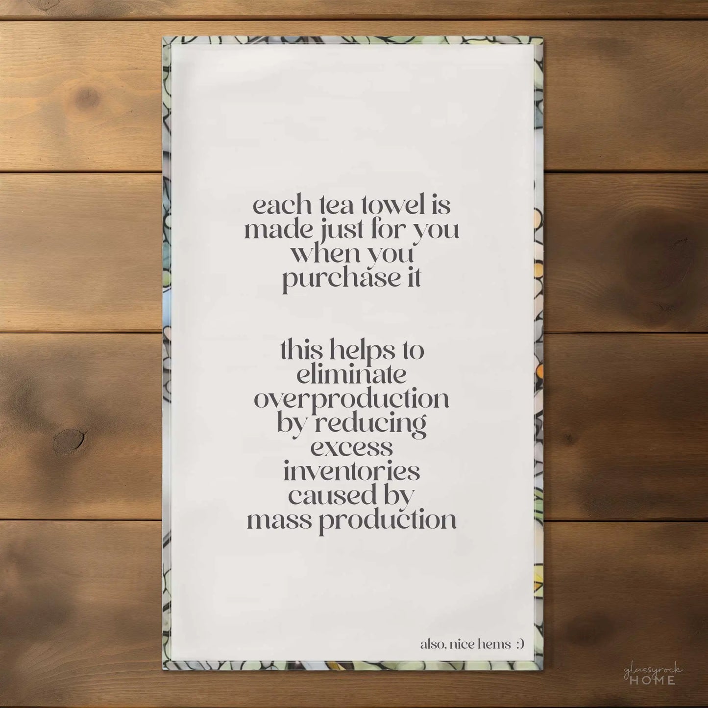 On a wooden surface, the Stained Glass Nouveau Ferns Dish Towel, crafted uniquely per order to curb excess inventory from mass production. Plus, nice hems!.