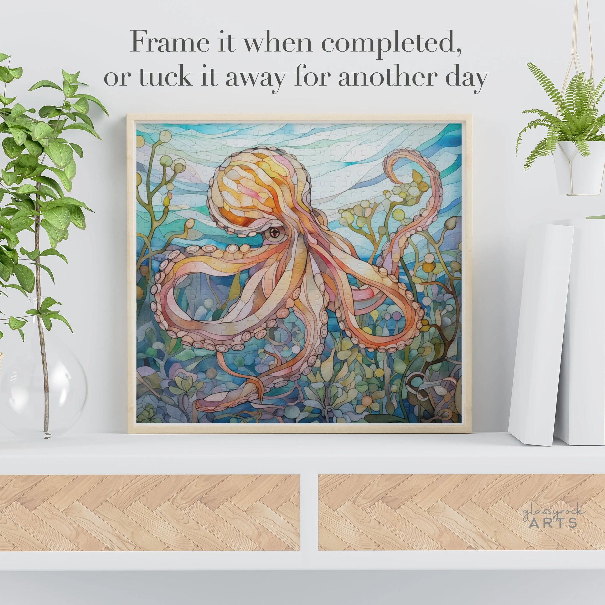 The Stained Glass Octopus Jigsaw Puzzle, with its intricate underwater octopus design, is framed and displayed on a shelf surrounded by plants. The message reads: Frame it when completed, or tuck it away for another day above this ocean-themed art piece.