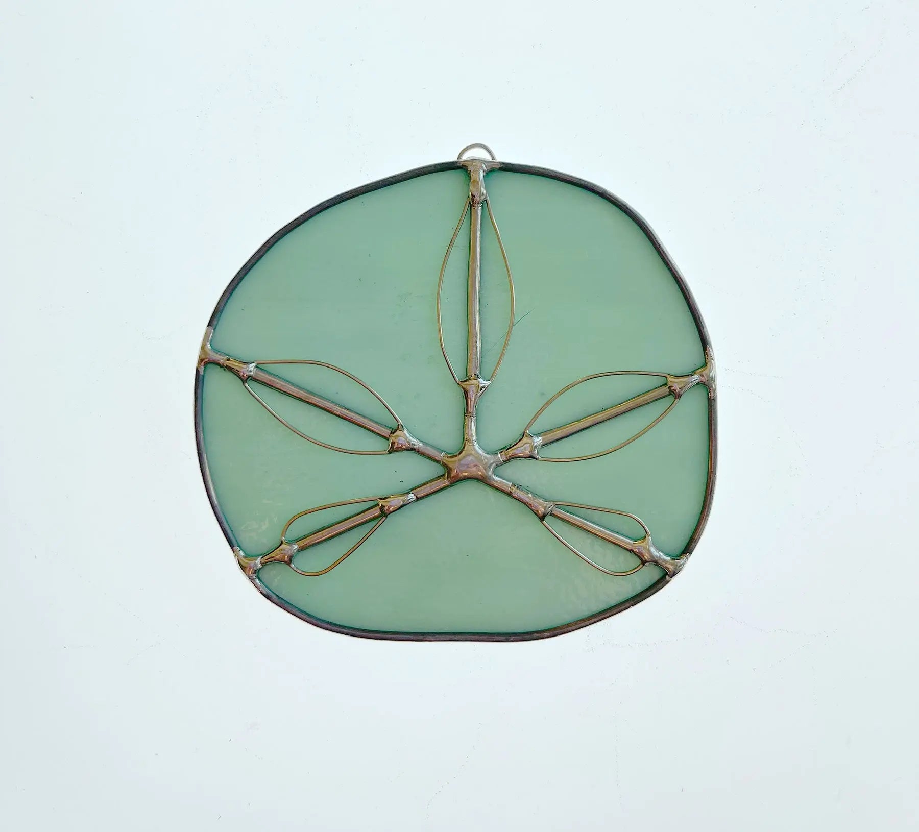 The Turquoise Handmade Stained Glass Sand Dollar, crafted by a Pacific Northwest artist, features wire outlines forming symmetrical leaf shapes in a minimalist and delicate design against a light background.