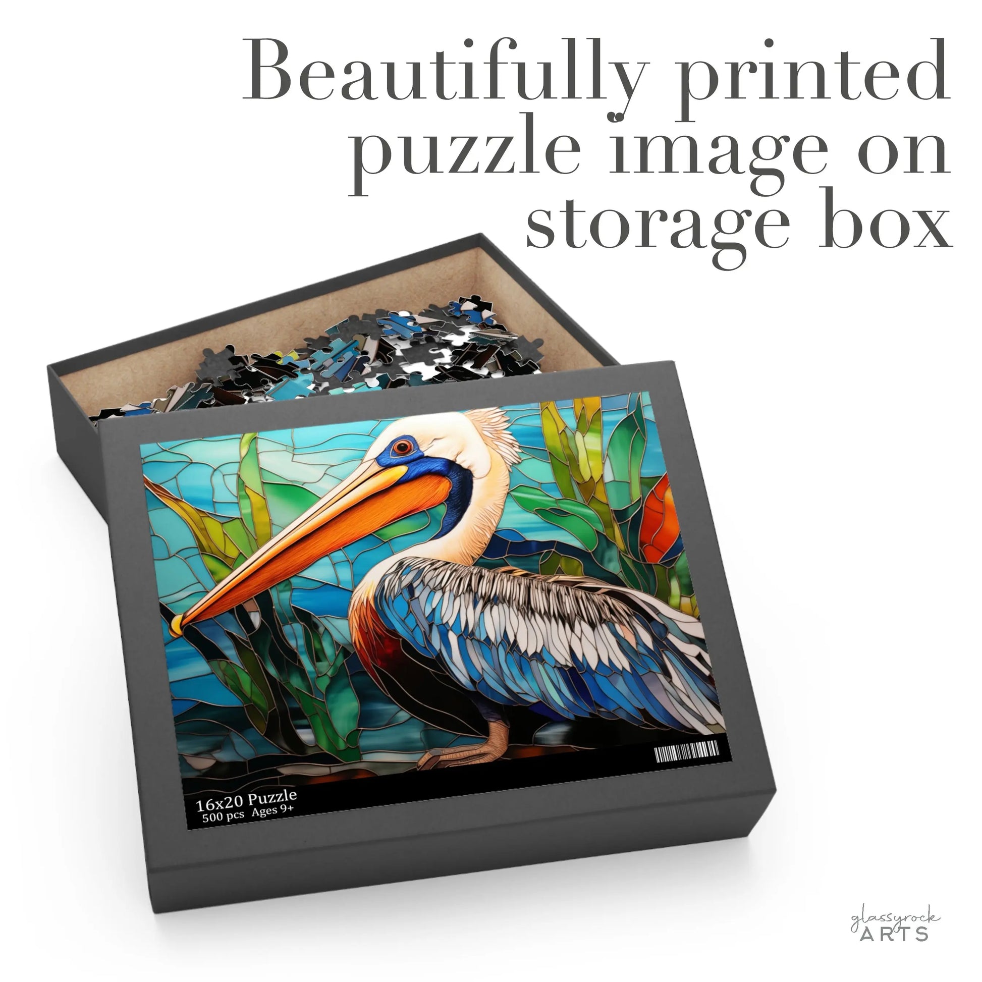 The Stained Glass Pelican Jigsaw Puzzle box, with its vibrant pelican image, is open and pieces are scattered inside. The text Beautifully printed puzzle image on storage box suggests its the perfect art gift for a couple.
