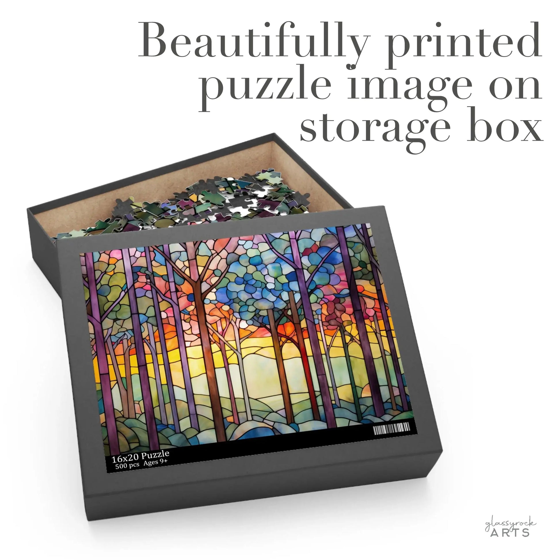 The Rainbow Forest Jigsaw Puzzle box showcases a stained glass-inspired abstract forest scene, with tall trees set against a vibrant sunrise or sunset sky. The open box reveals partially completed puzzle pieces, with text stating Beautifully printed puzzle image on storage box.