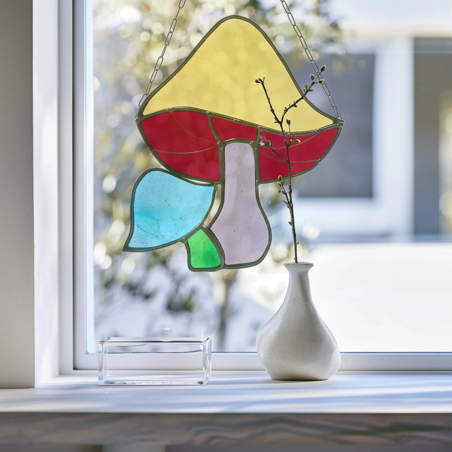 A Handmade Stained Glass Rainbow Mushroom by a Pacific Northwest artist casts colorful reflections. Next to it, a minimalist white vase with a branch enhances the natural serenity.