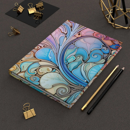 The Rainbow Paisley Stained Glass Hardcover Journal rests on a textured black surface, accompanied by gold binder clips, a black pencil, a gold pencil, and adorned with a gold geometric decor piece in the corner.