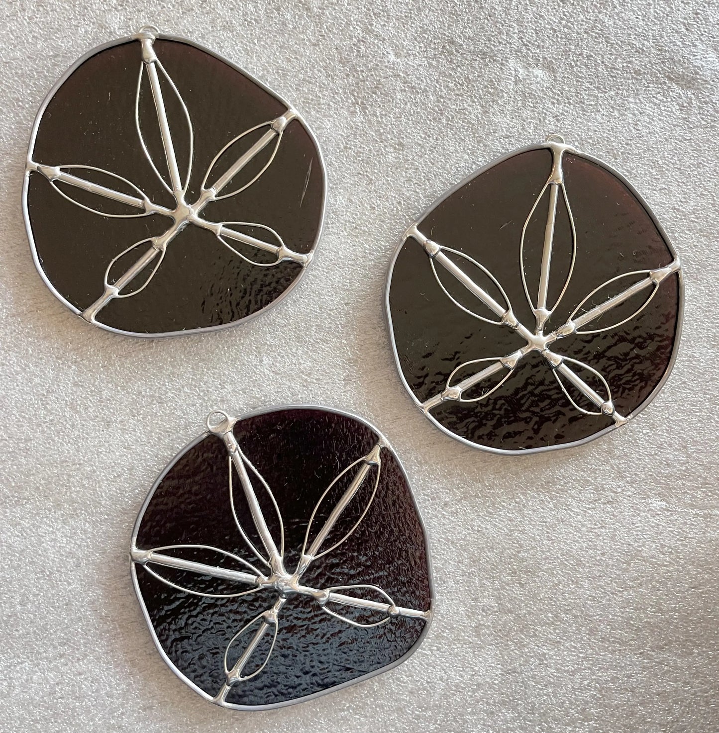 Three purple handmade stained glass sand dollars with handworked wire accents
