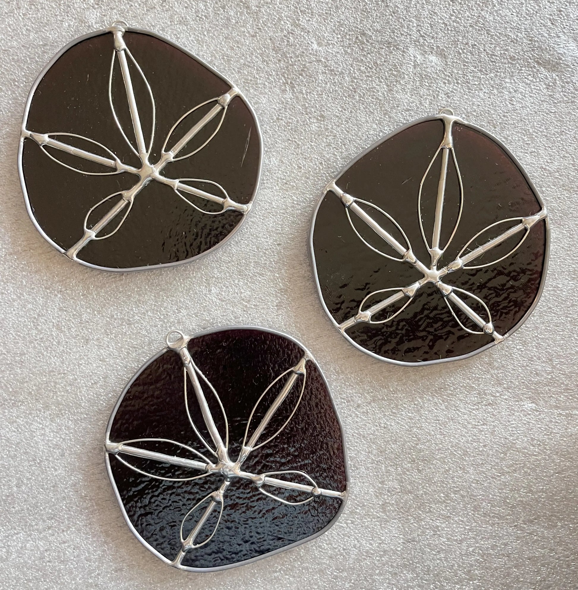 Three purple handmade stained glass sand dollars with handworked wire accents