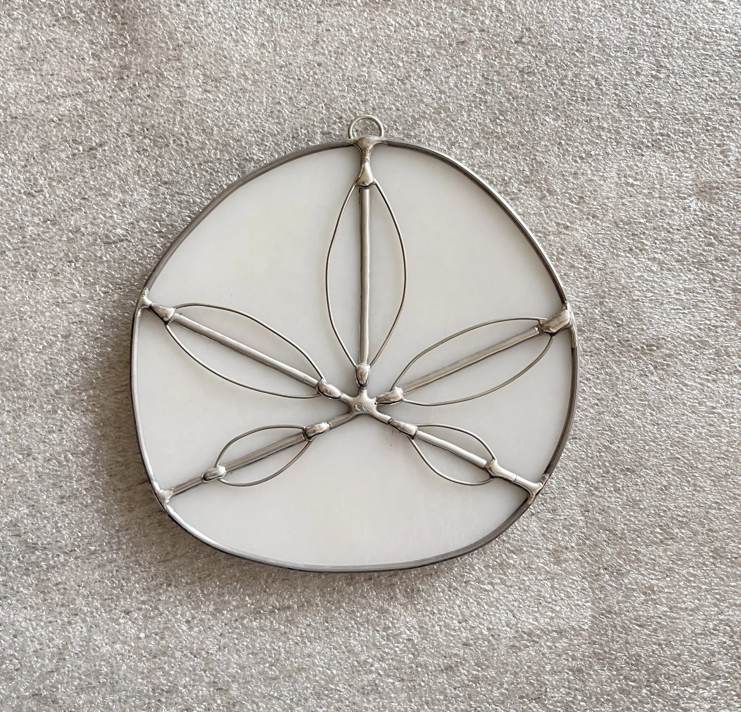 Handmade Stained Glass Sand Dollars - White, made from metal and white material with leaf-shaped cutouts, reflect a Pacific Northwest artists craftsmanship, displayed on a textured beige surface.
