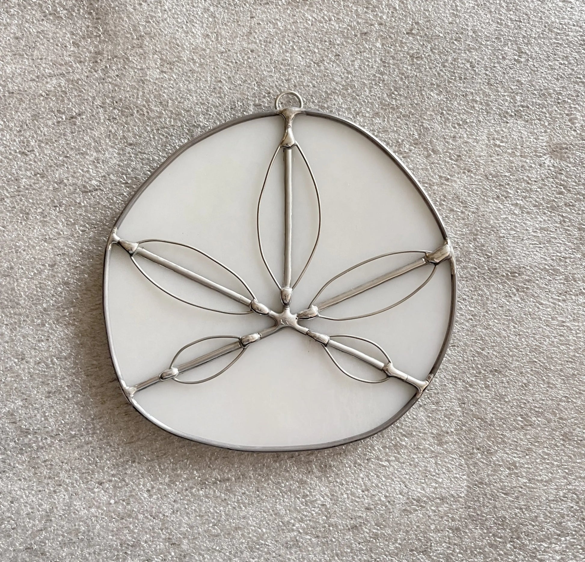 Handmade Stained Glass Sand Dollars - White, made from metal and white material with leaf-shaped cutouts, reflect a Pacific Northwest artists craftsmanship, displayed on a textured beige surface.