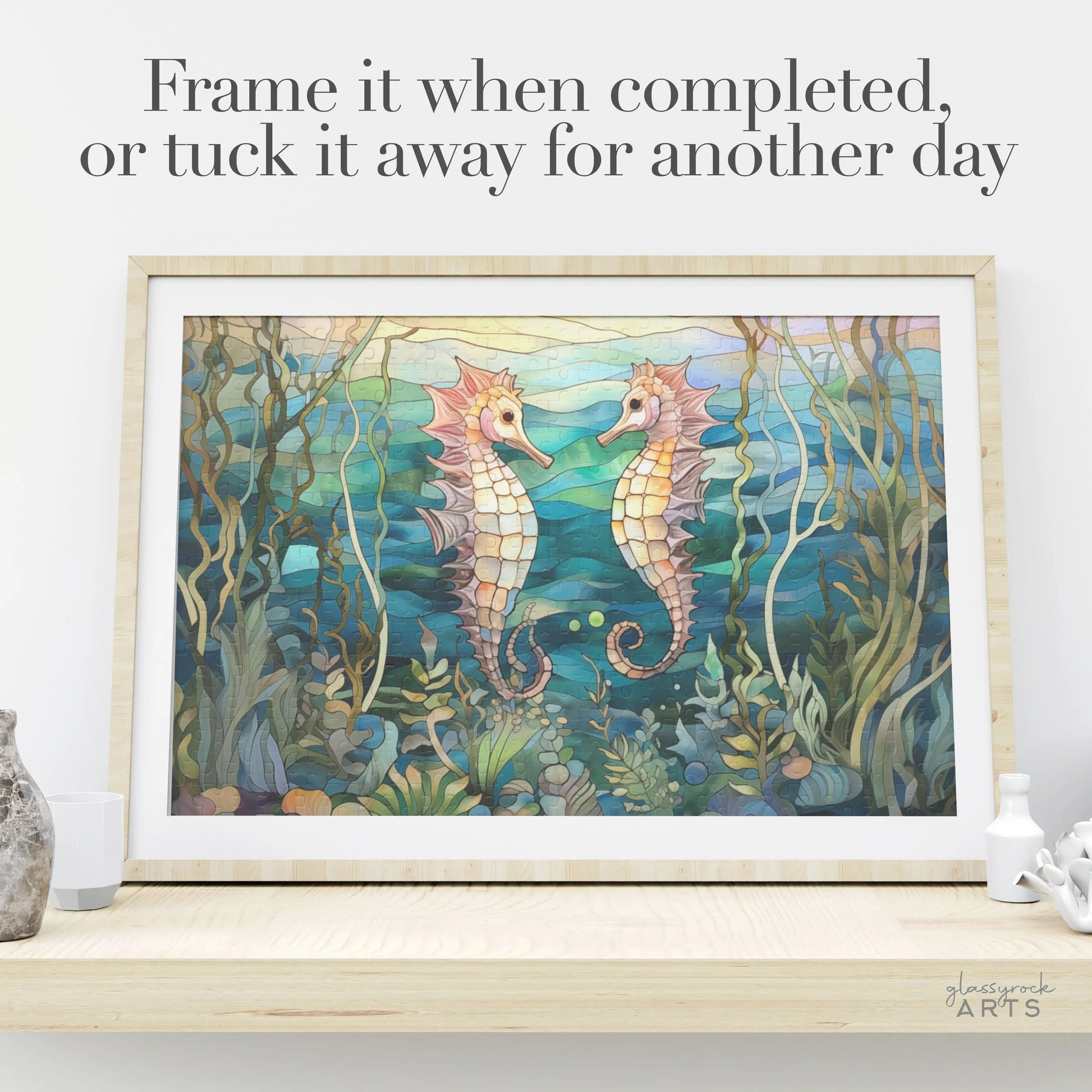 The Stained Glass Seahorses Jigsaw Puzzle showcases two seahorses facing each other amid vibrant ocean plants. Ideal for nature lovers, the puzzle is displayed on a light wooden shelf with decor. Above, text reads, Frame it when done or save for later.