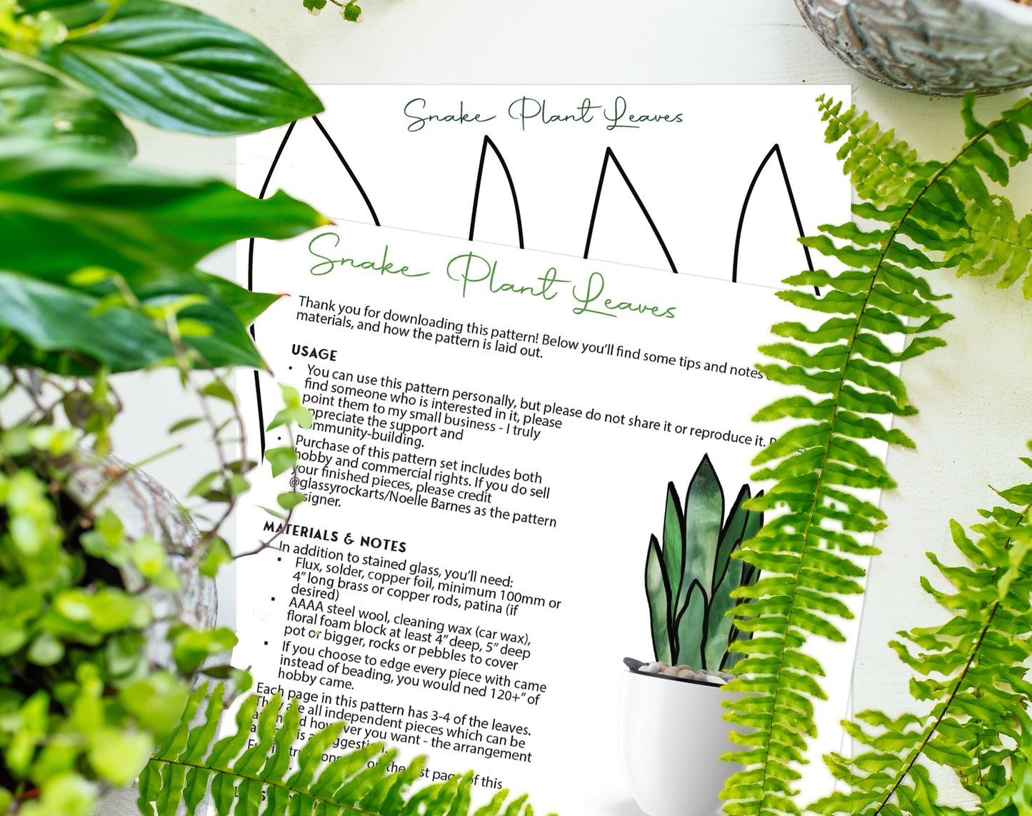 The 3D Snake Plant Leaves Stained Glass Pattern guide, surrounded by lush green plants and ferns, includes detailed usage instructions and required materials. A small potted plant is at the bottom right, enhancing the bright and vibrant scene.