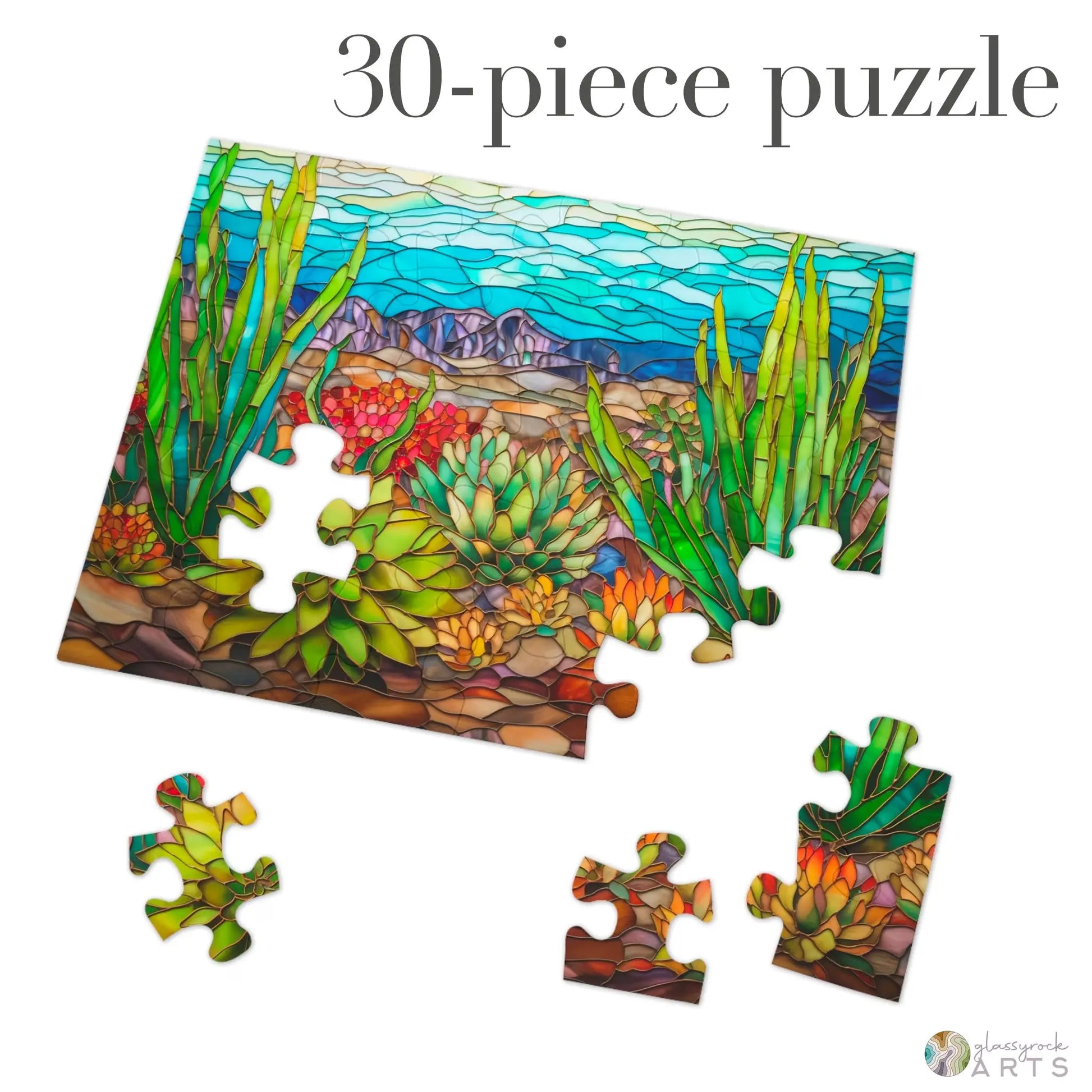 The Stained Glass Succulents Jigsaw Puzzle, a 30-piece set, features a vibrant desert scene with cacti and mountains against a blue sky. Several pieces are scattered around the main puzzle, making it an ideal gift-ready choice.